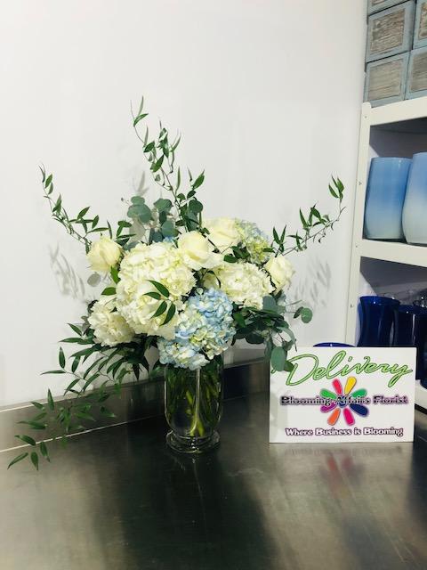 White and pale blue flowers in a glass vase with long greenery
