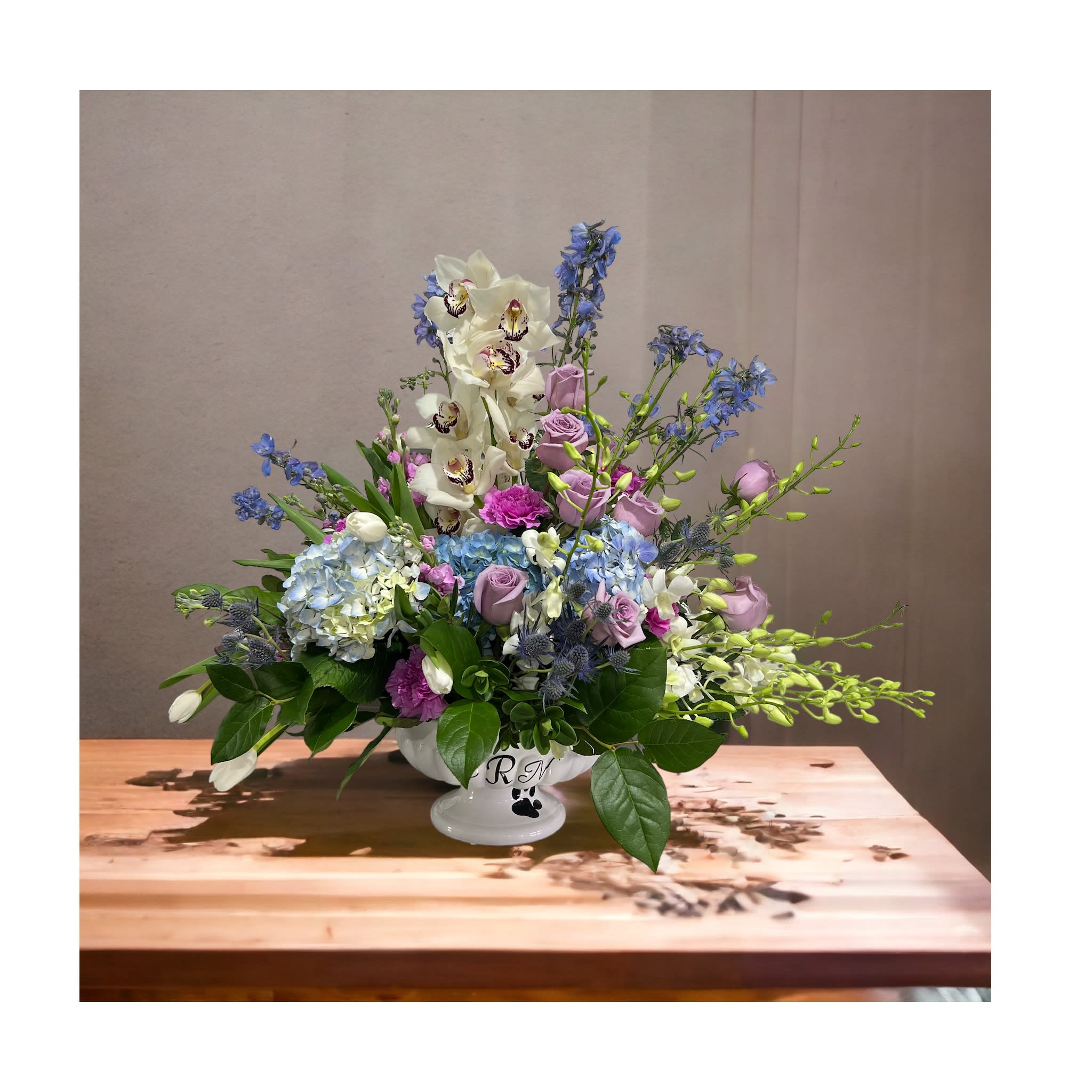Lavender, blue, and white floral arrangement in a white pedestal vase