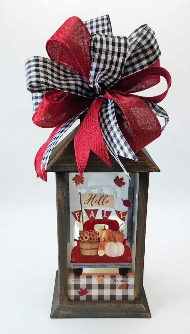 Wooden lantern with a large red and black plaid bow and fall-themed insert