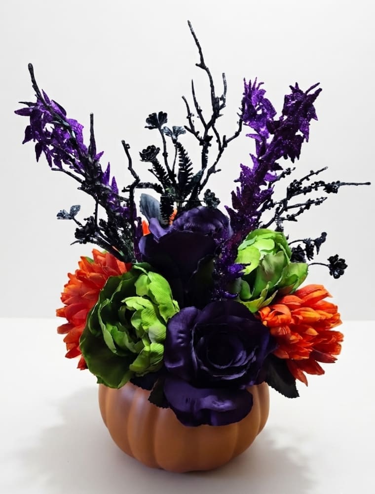 Purple, green, and orange floral arrangement in a pumpkin-shaped container