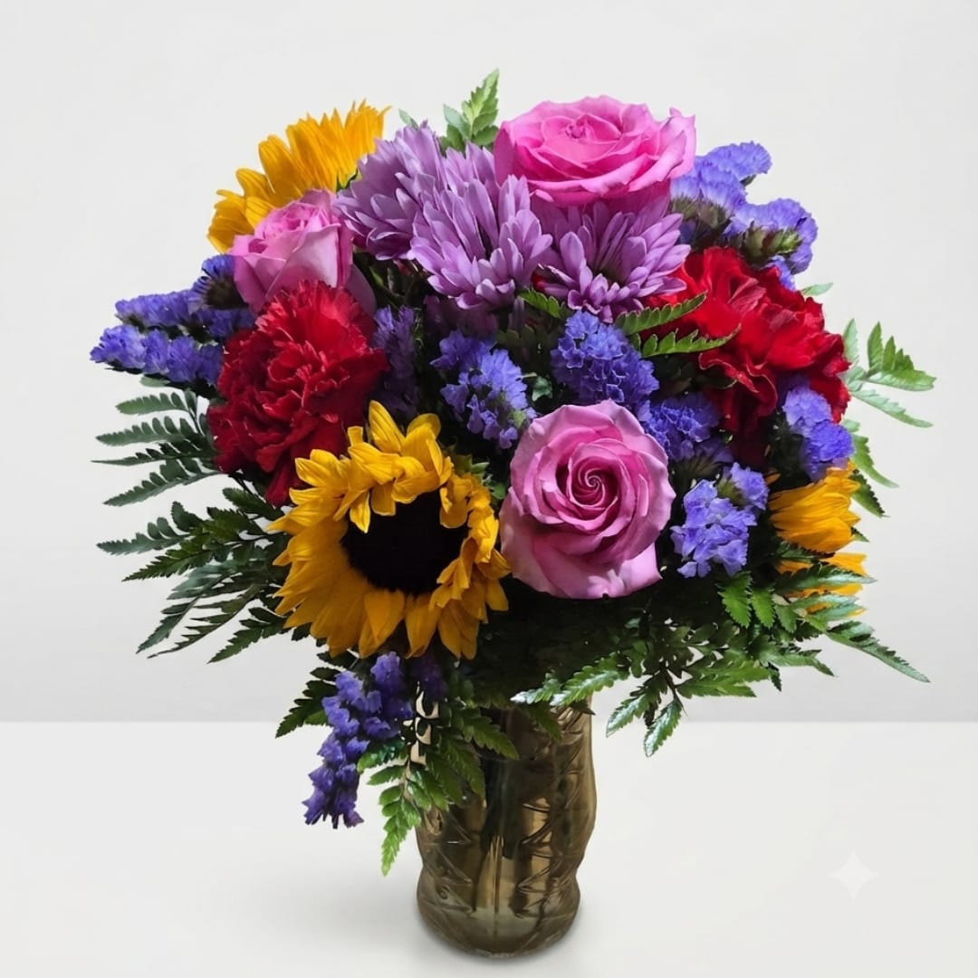 Mixed bouquet of roses, sunflowers, carnations, and purple blooms in a glass vase