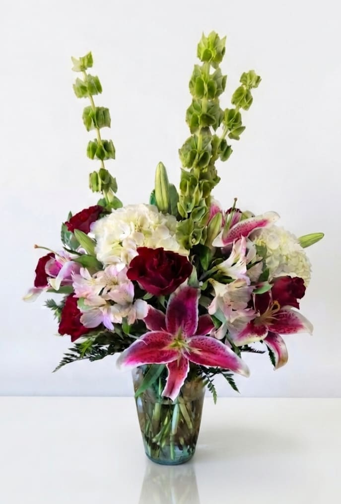 Mixed bouquet of lilies, hydrangeas, and red blooms in a glass vase