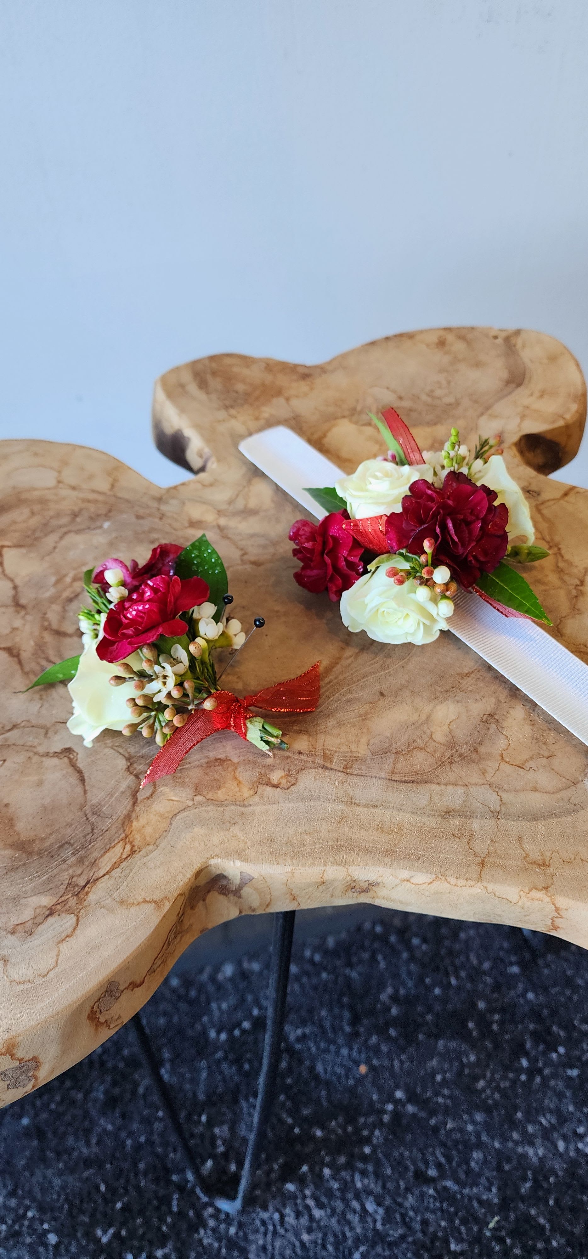 Two floral boutonnieres with red and white roses on a wooden surface