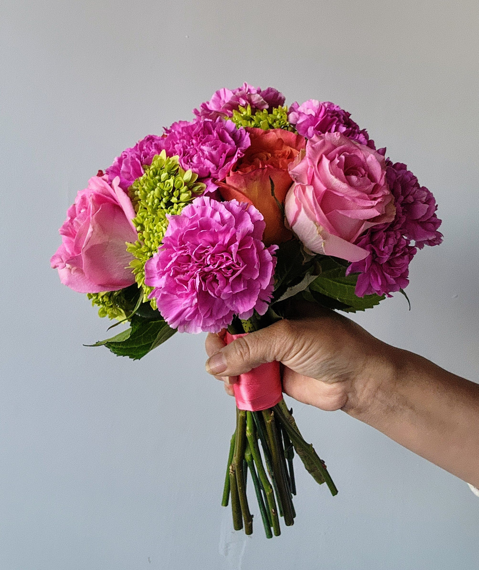 Handheld bouquet of pink roses and carnations with green accents