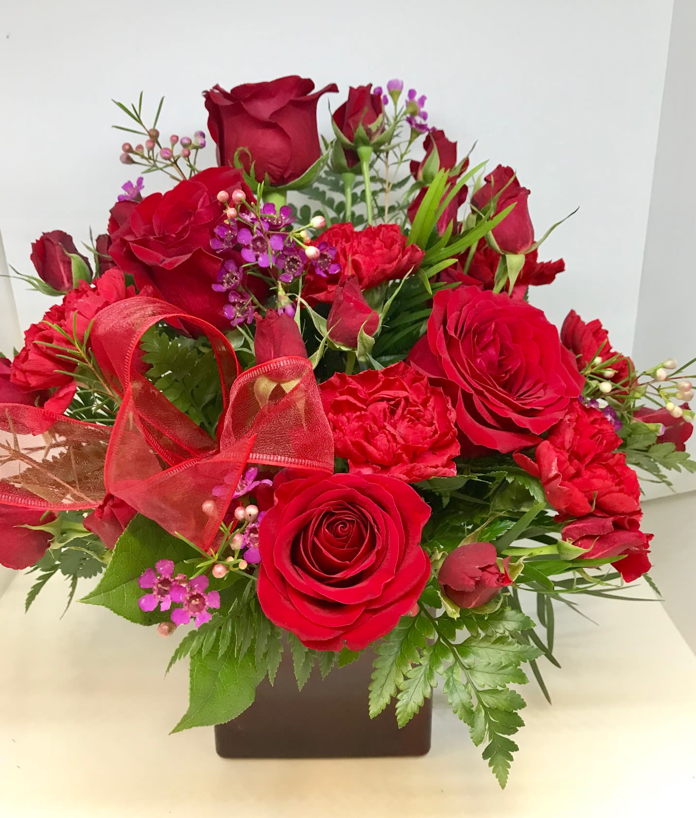 Red roses and carnations in a square vase with a red ribbon