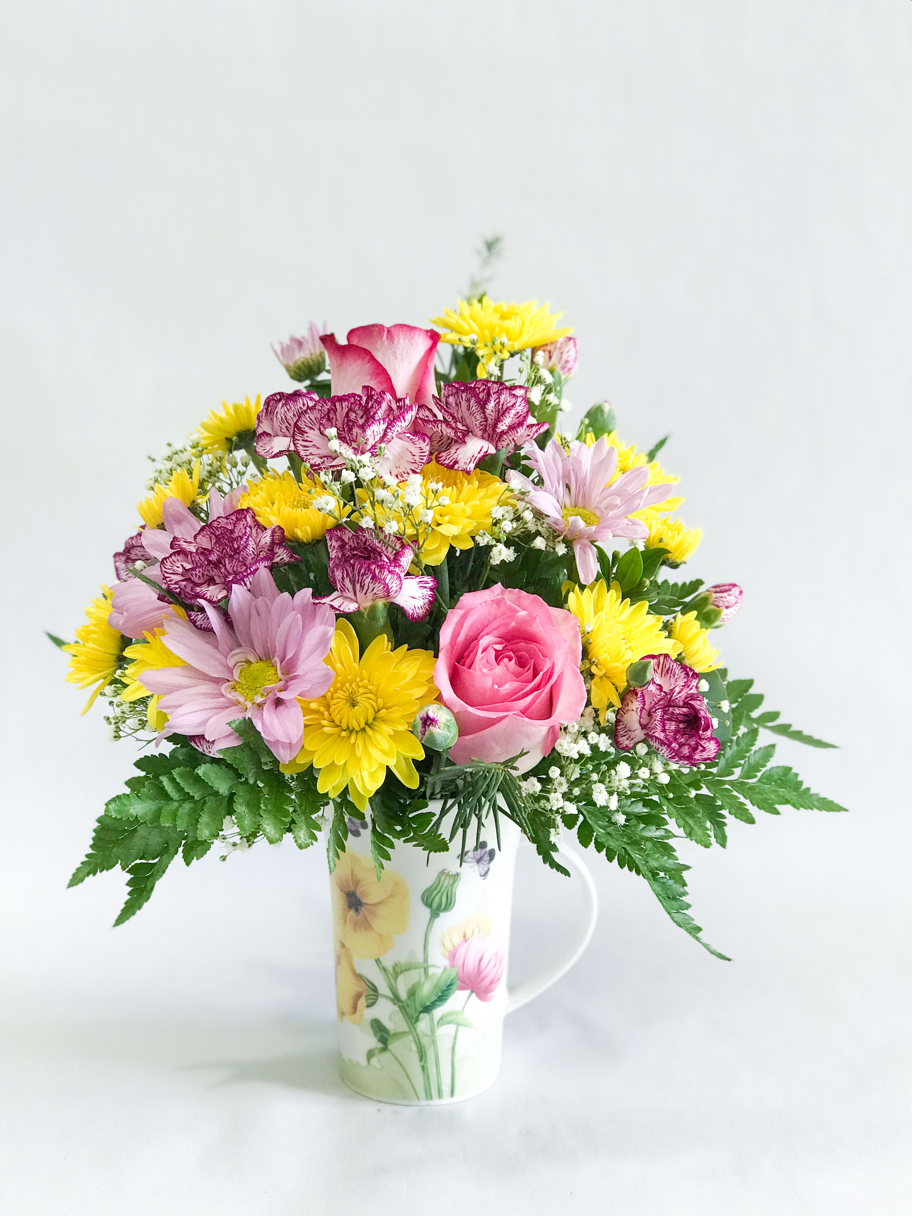 Mixed bouquet in a floral mug vase with pink, yellow, and purple blooms