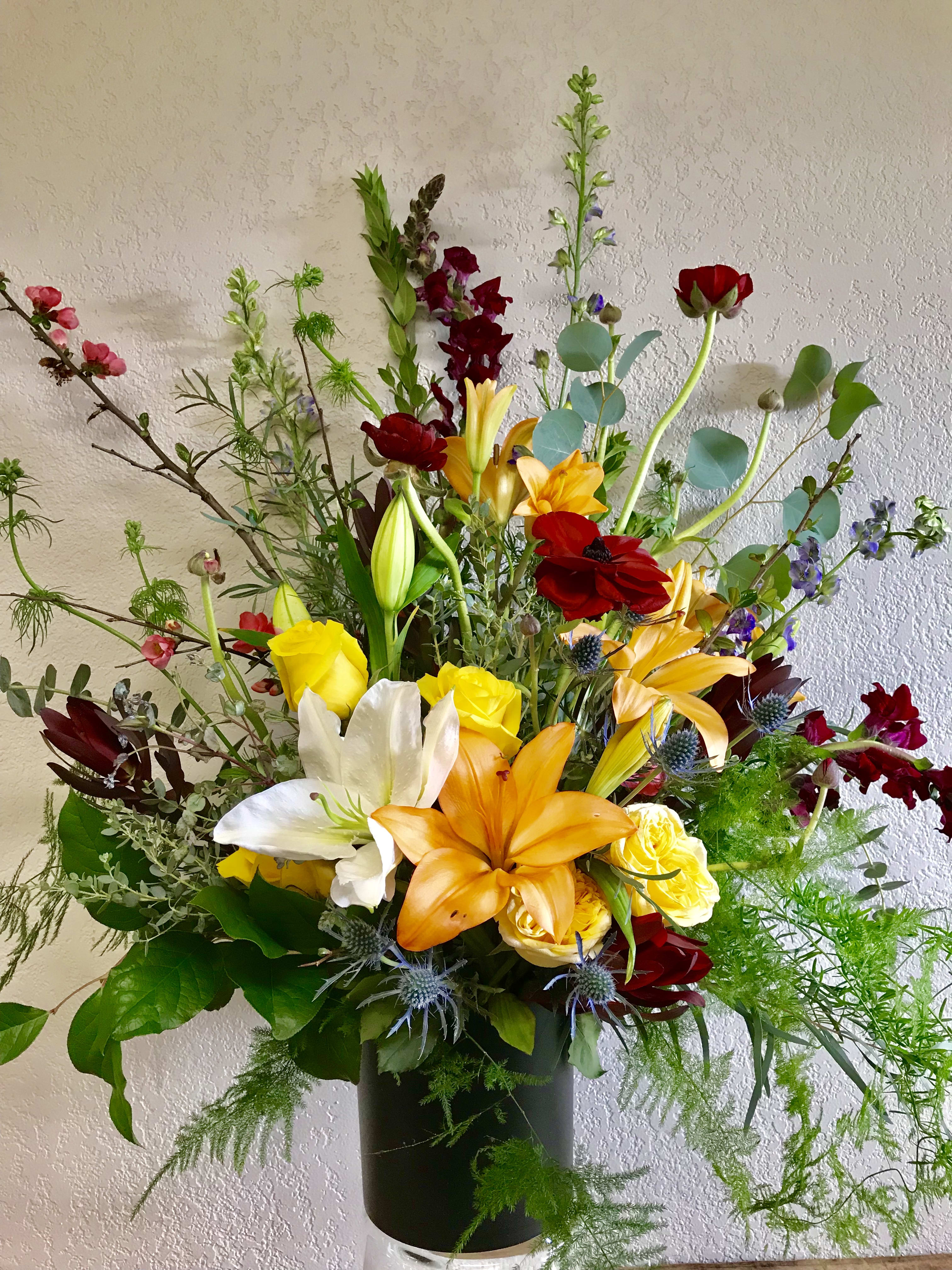 Tall mixed bouquet with lilies, roses, and red blooms in a black vase