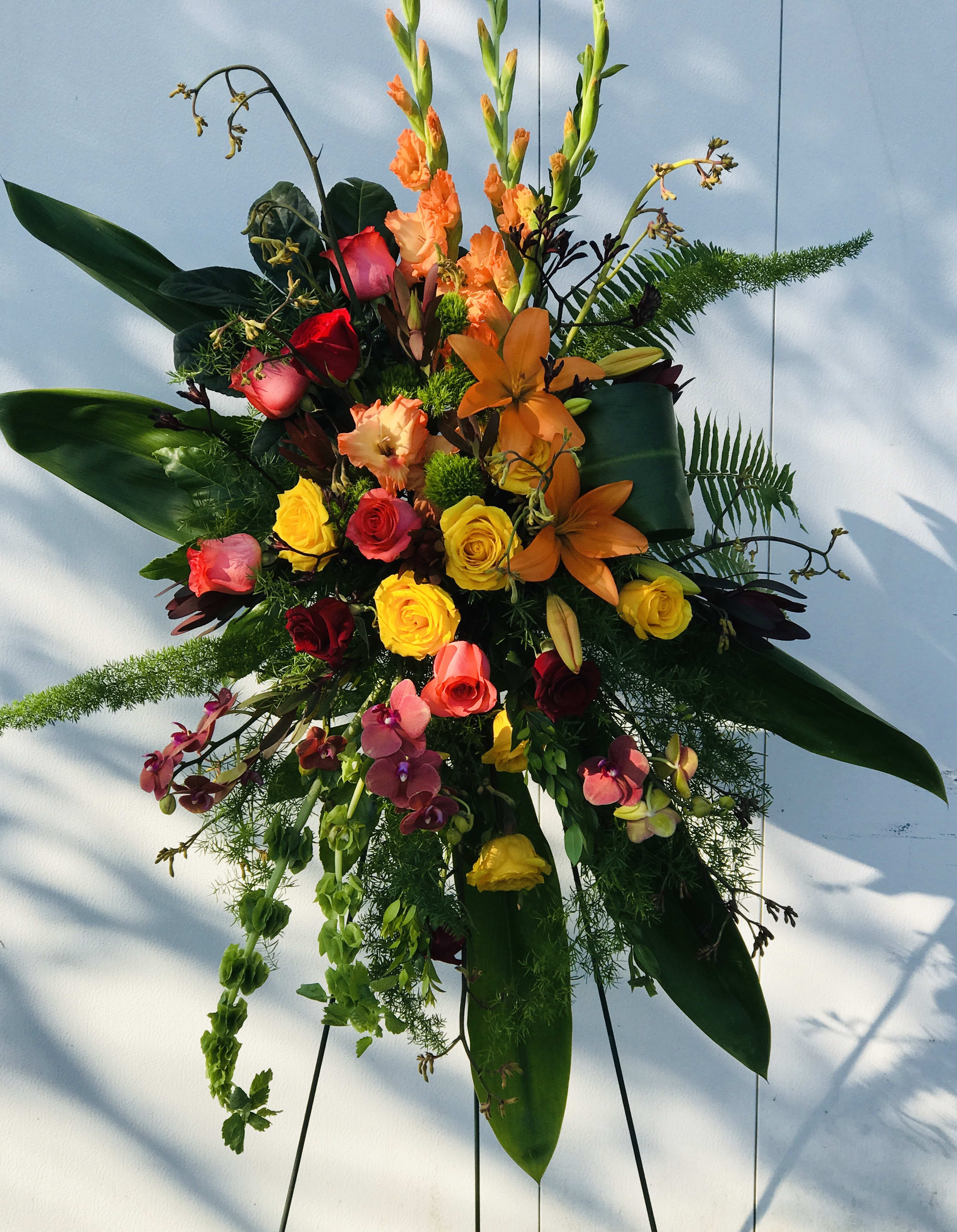 Tall mixed floral spray with roses, lilies, orchids, and orange blooms
