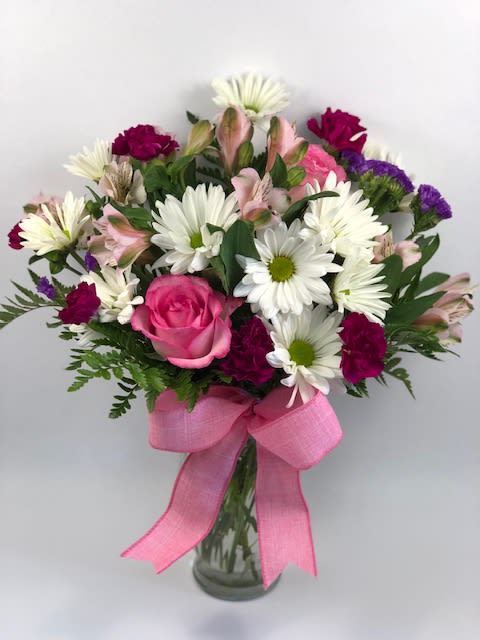 Bouquet of pink roses, white daisies, and mixed blooms in a glass vase with a pink ribbon