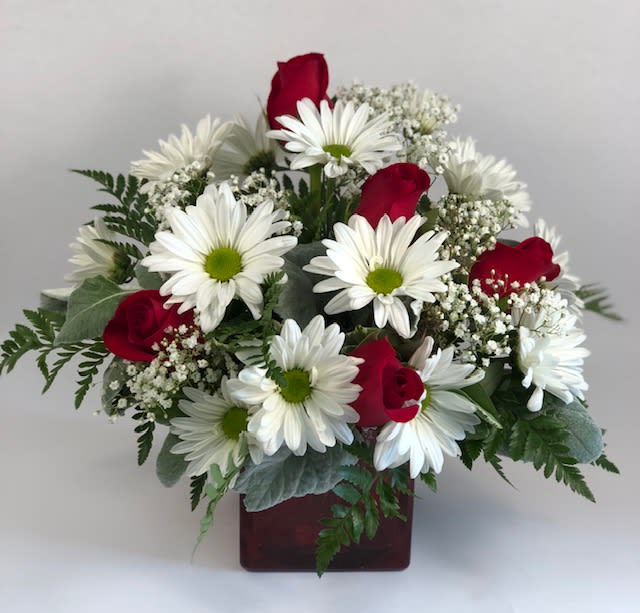 Bouquet of white daisies and red roses in a square vase