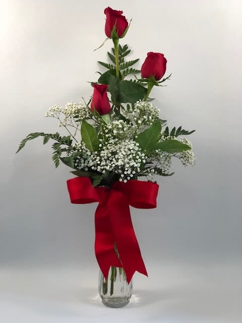 Tall bouquet of red roses with baby's breath in a glass vase and red ribbon