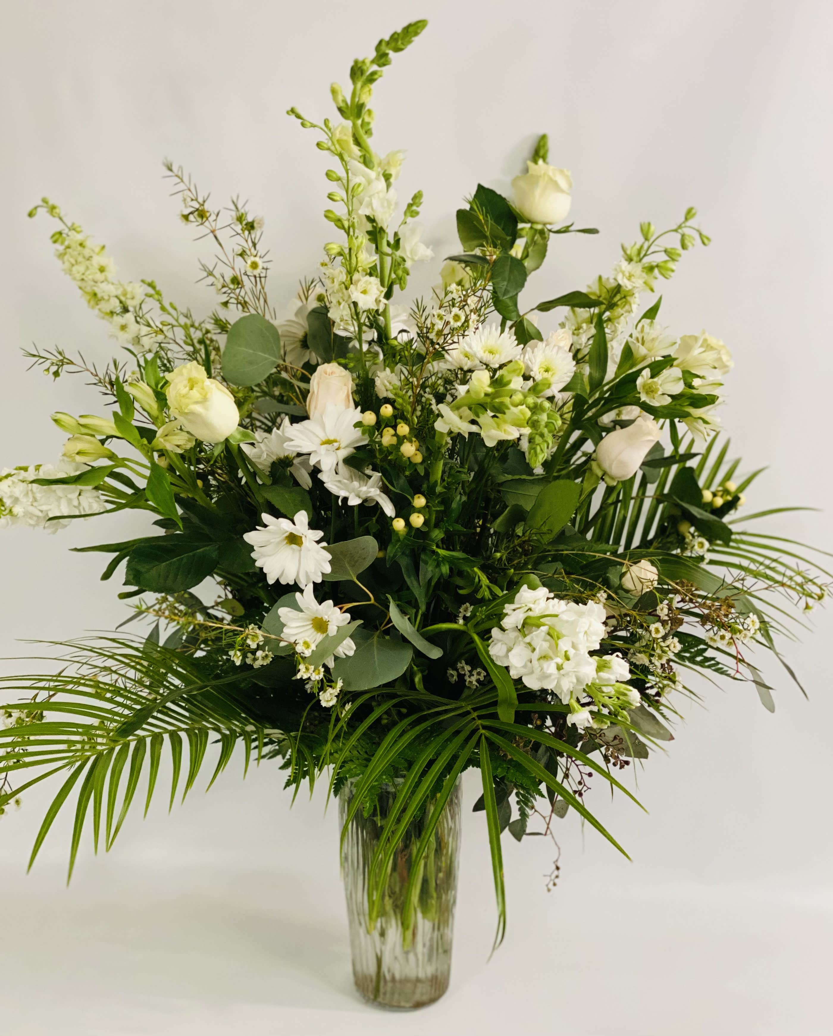 White floral arrangement in a clear glass vase with tall greenery