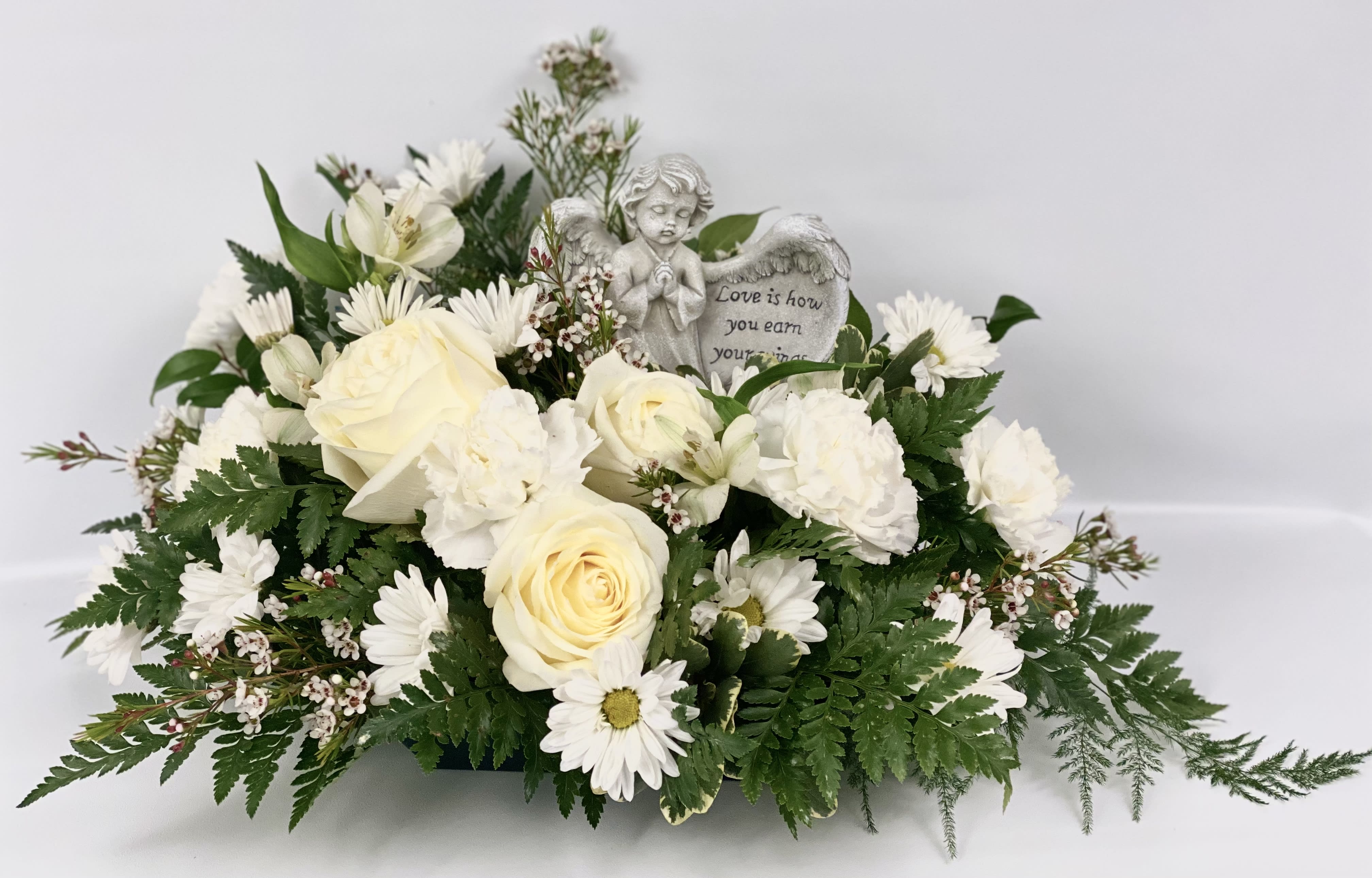 White floral arrangement with roses and daisies around an angel figurine