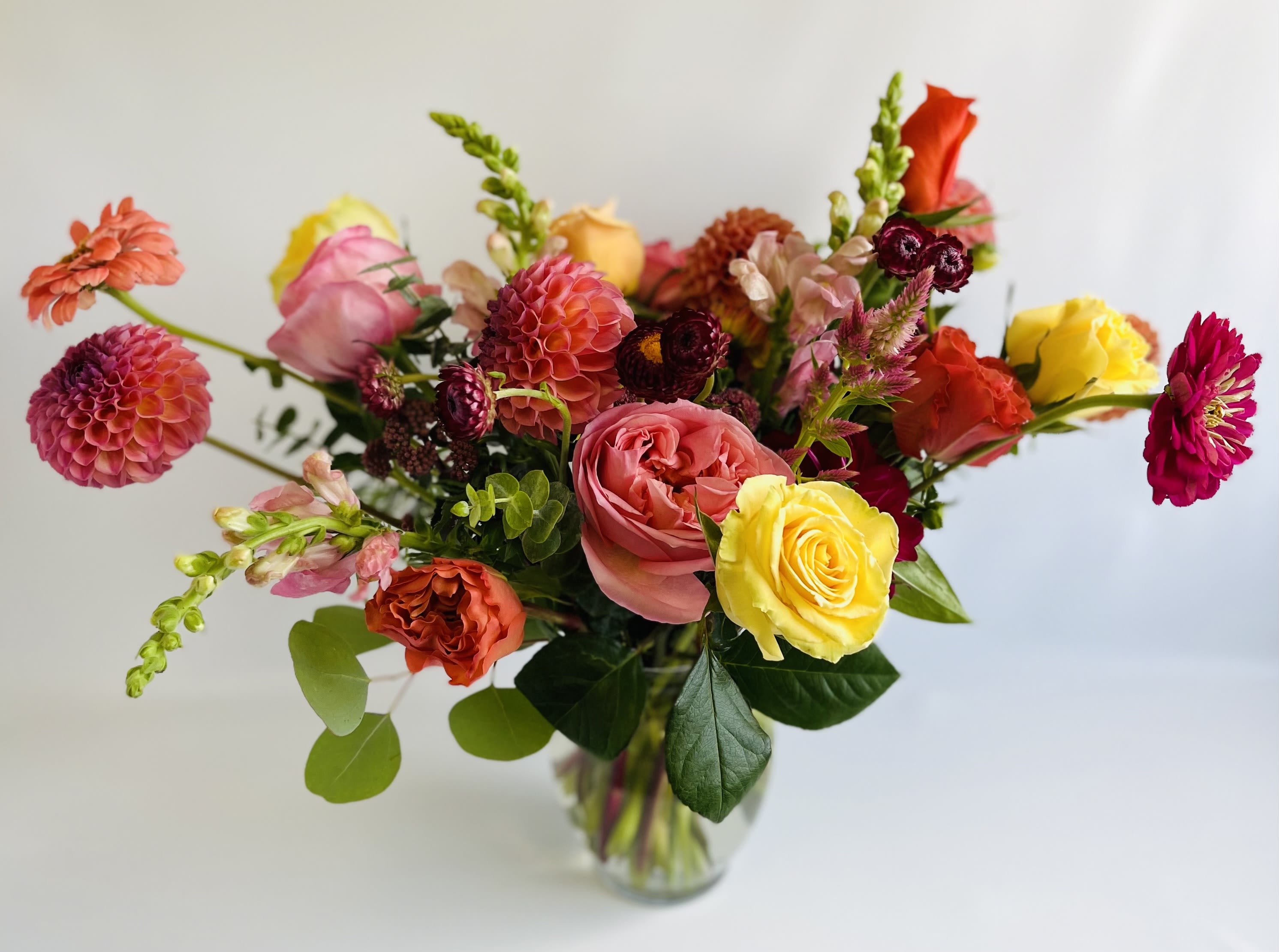 Mixed bouquet of roses, dahlias, and zinnias in a clear glass vase