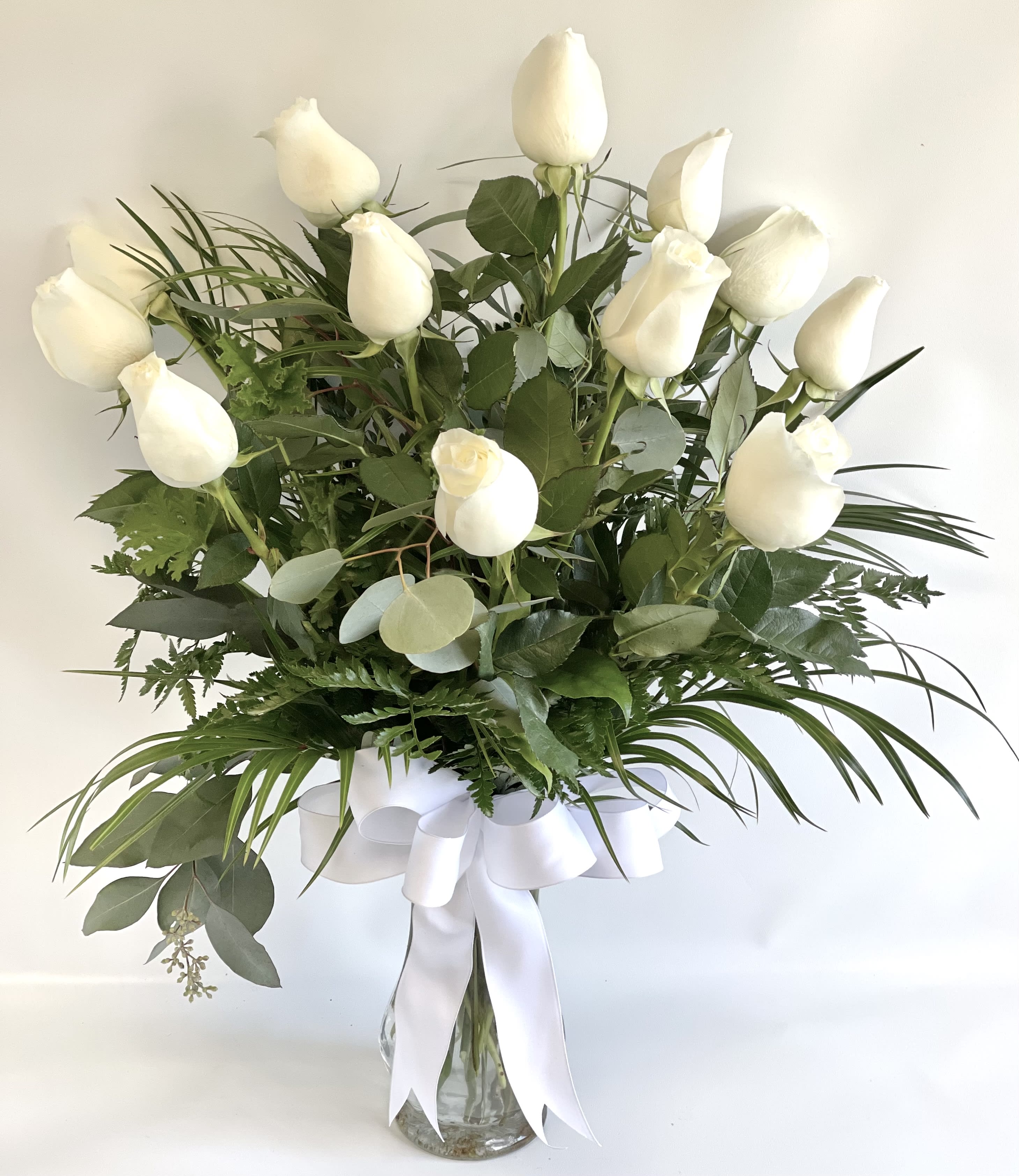 White roses in a glass vase with a white ribbon