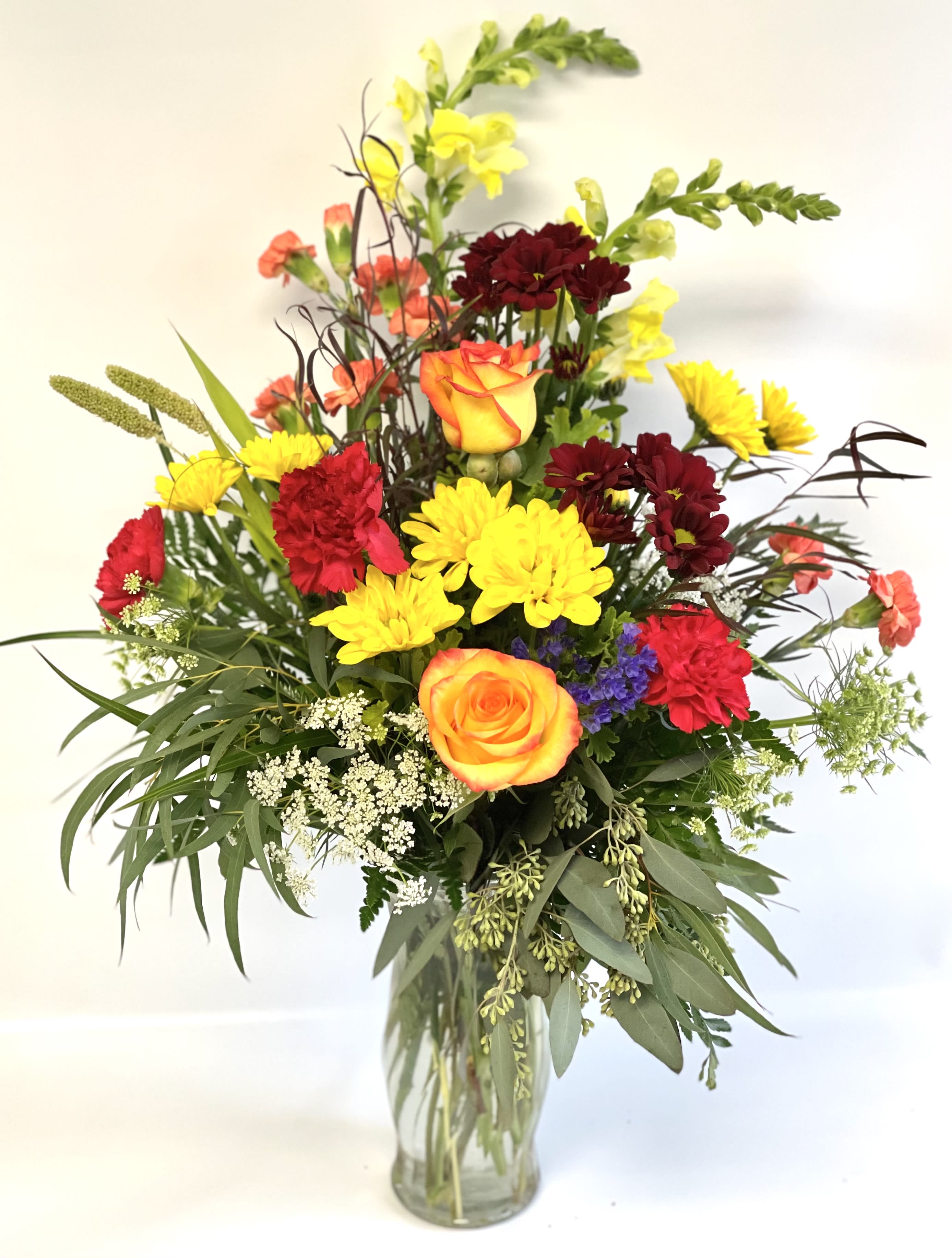 Mixed bouquet of roses, carnations, and yellow blooms in a glass vase