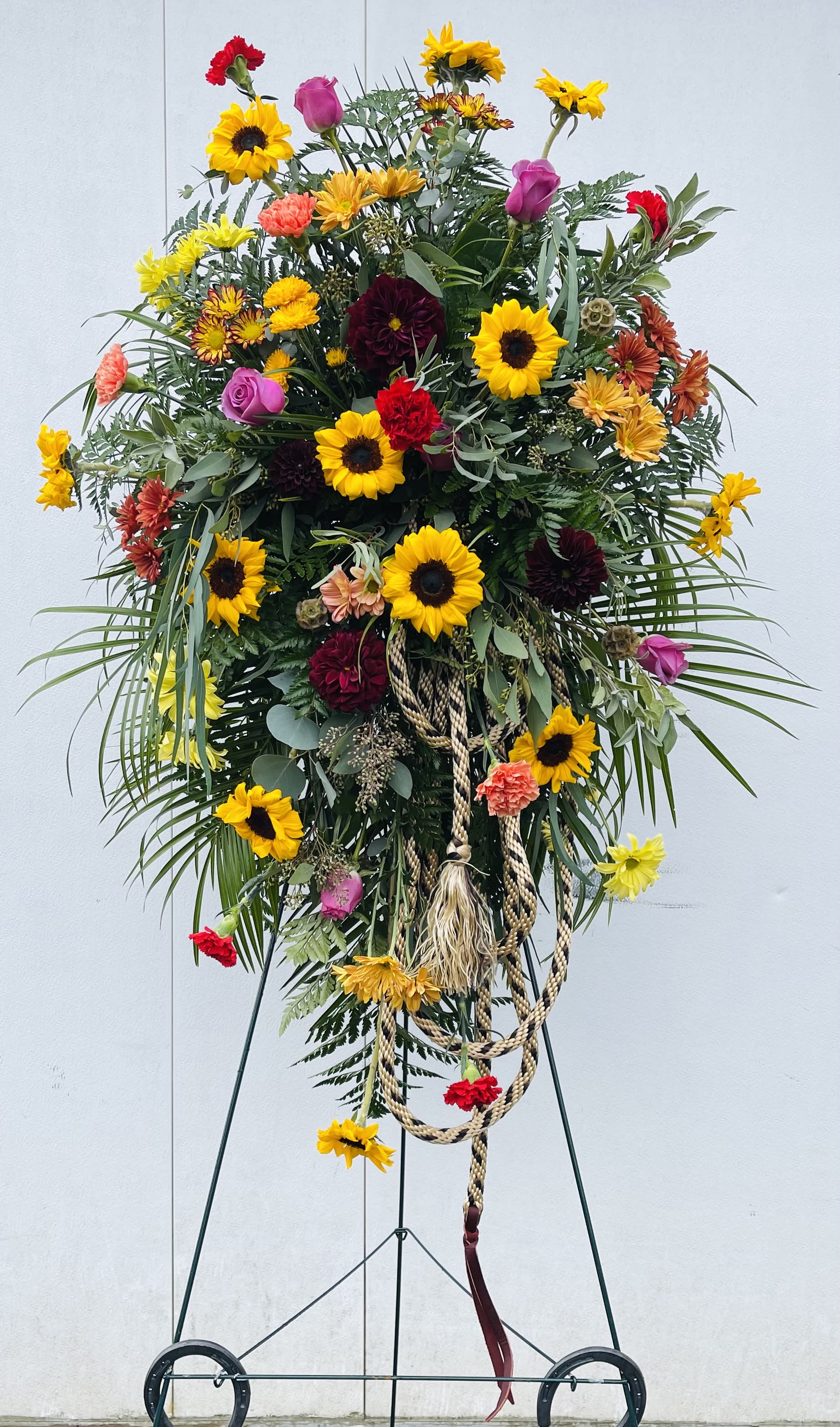 Tall floral standing spray with sunflowers, roses, and carnations on an easel