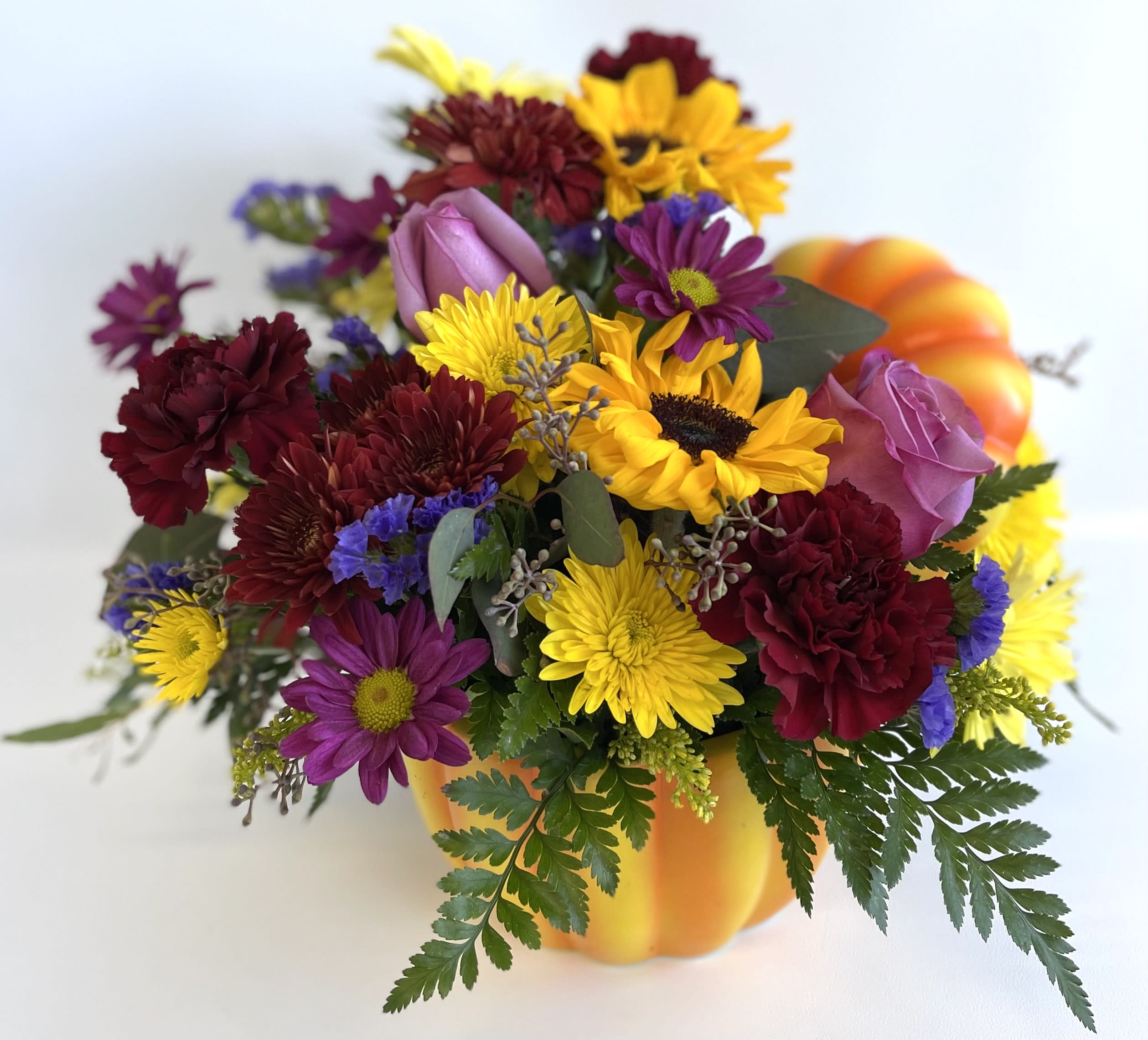 Mixed bouquet in a pumpkin-shaped container with yellow, purple, and burgundy flowers