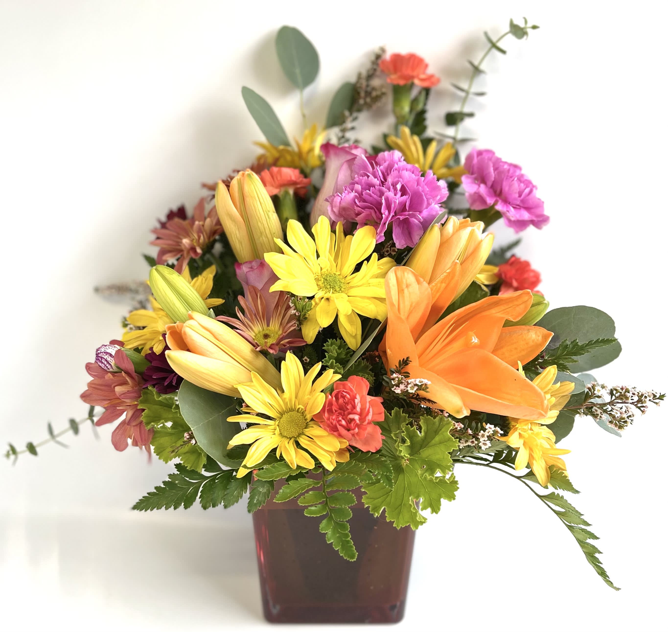 Mixed bouquet in a square vase with orange lilies and yellow daisies