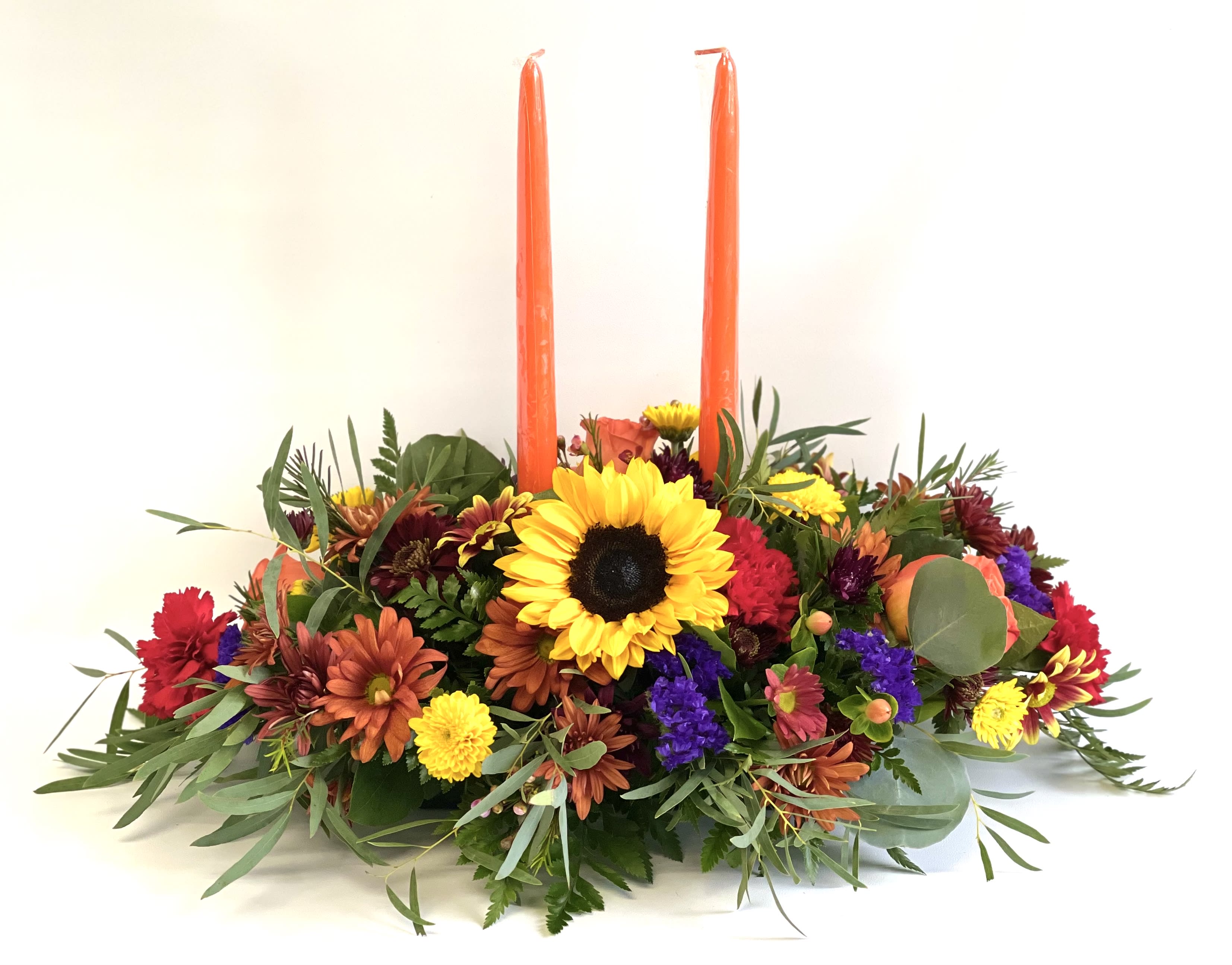 Low floral centerpiece with two tall orange candles and a sunflower