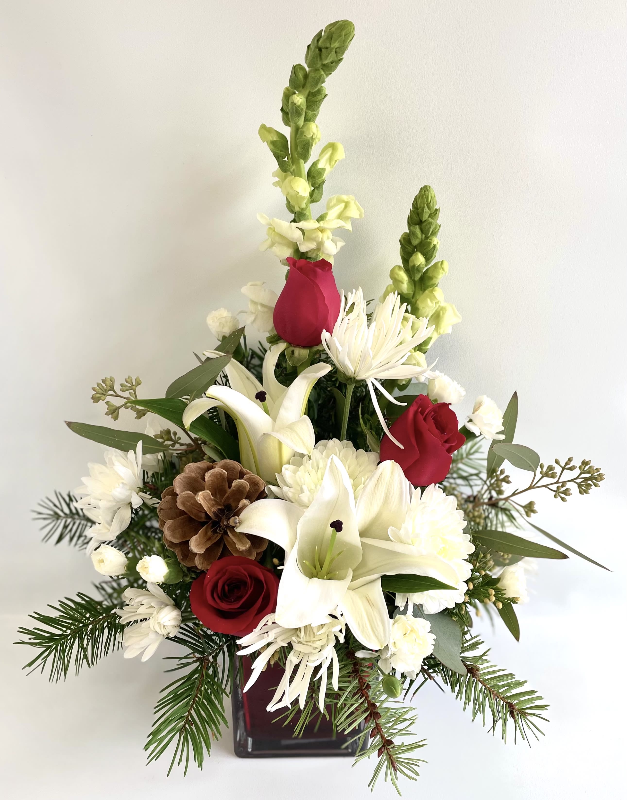Red roses and white lilies in a square vase with pinecones