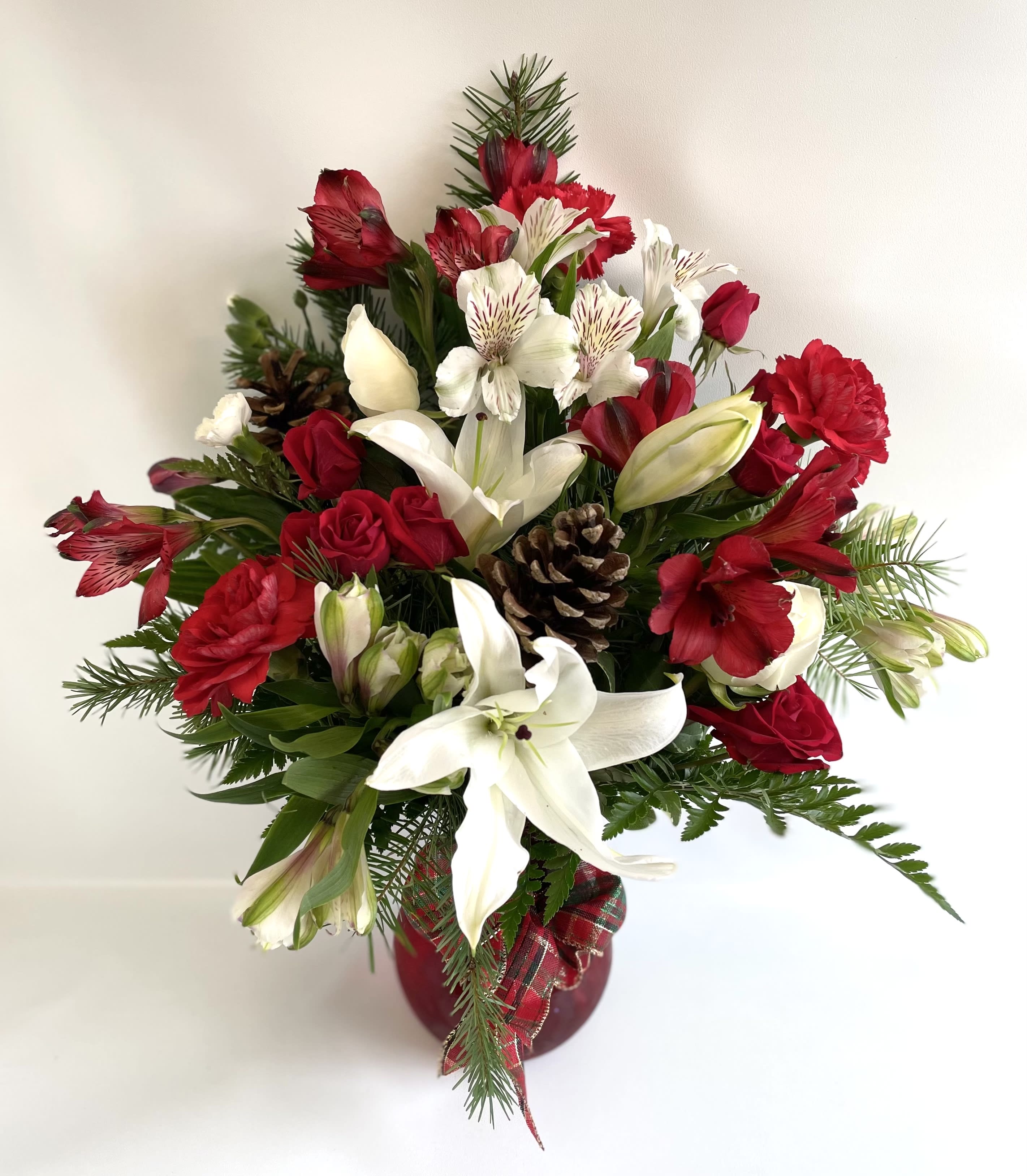 Red and white floral arrangement in a red vase with pinecones
