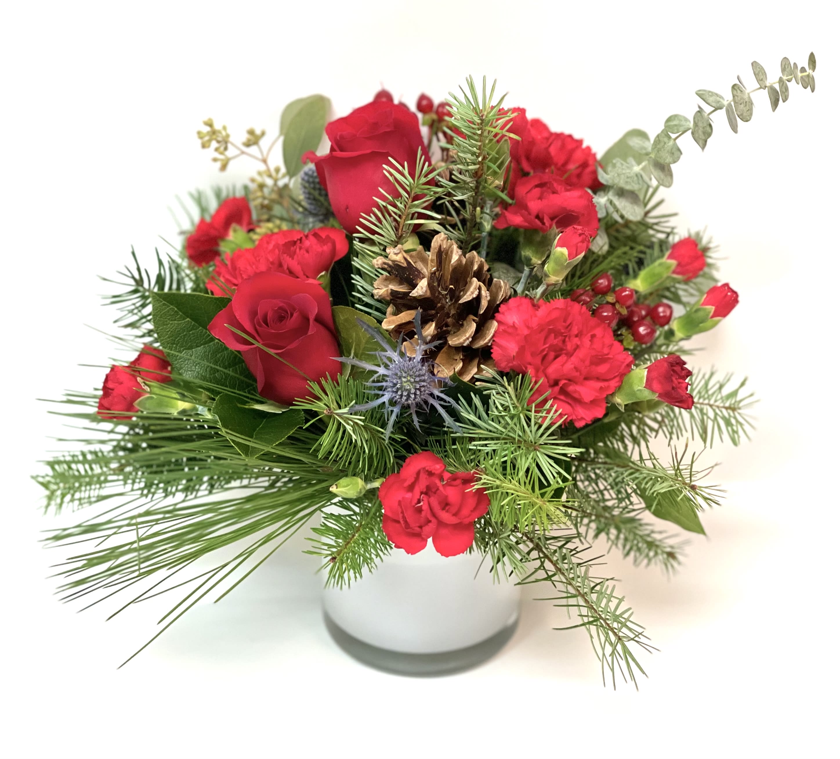 Red roses and carnations in a white vase with pine and a pinecone