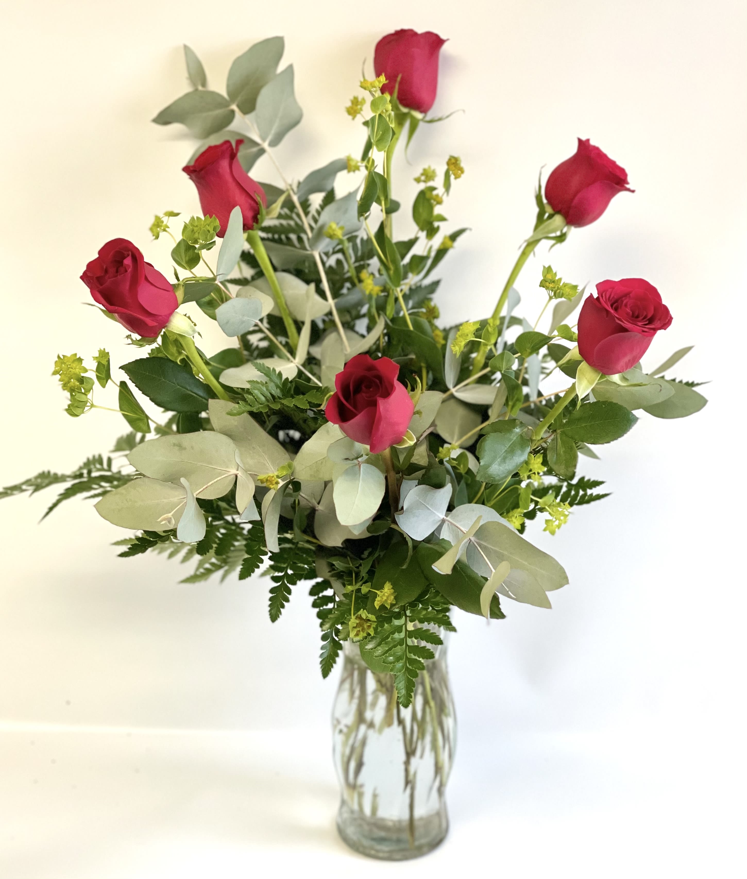 Red roses in a clear glass vase with mixed greenery