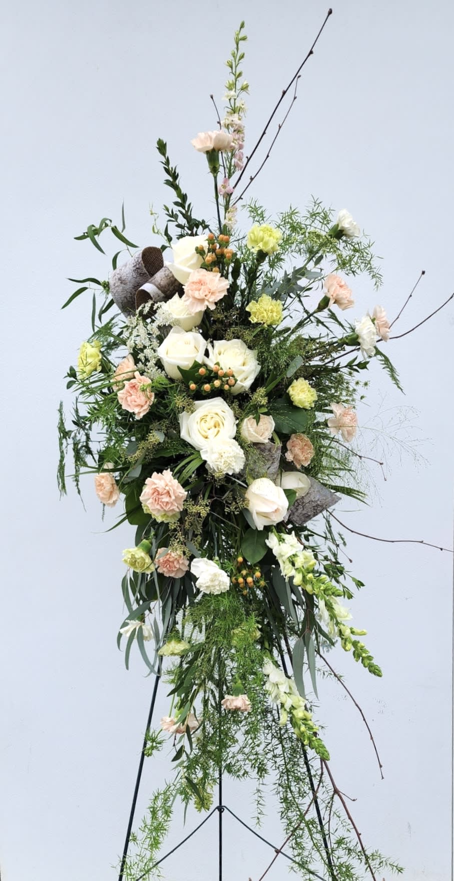 Tall floral standing spray with white and peach blooms on a metal easel