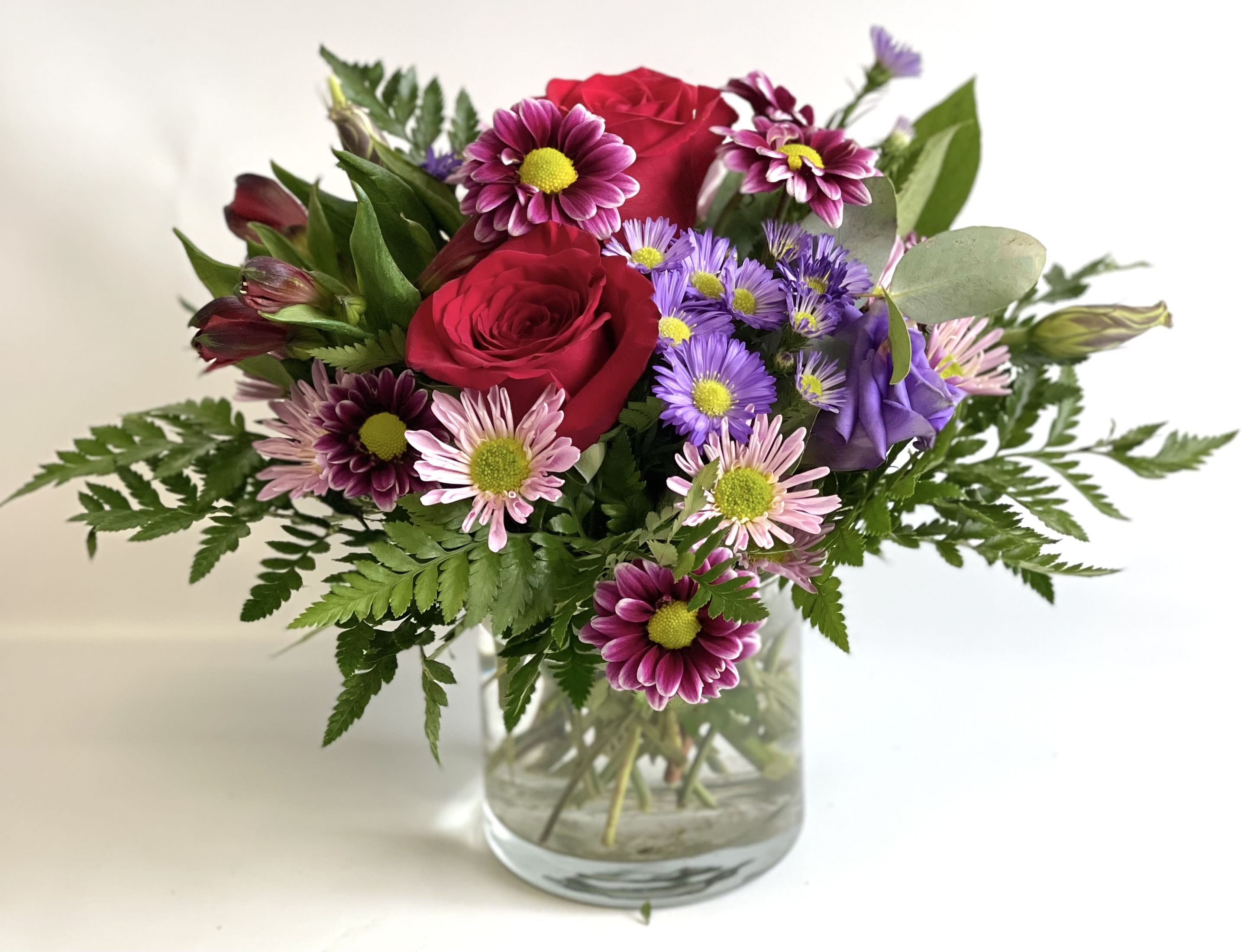 Bouquet of red roses and purple daisies in a glass vase
