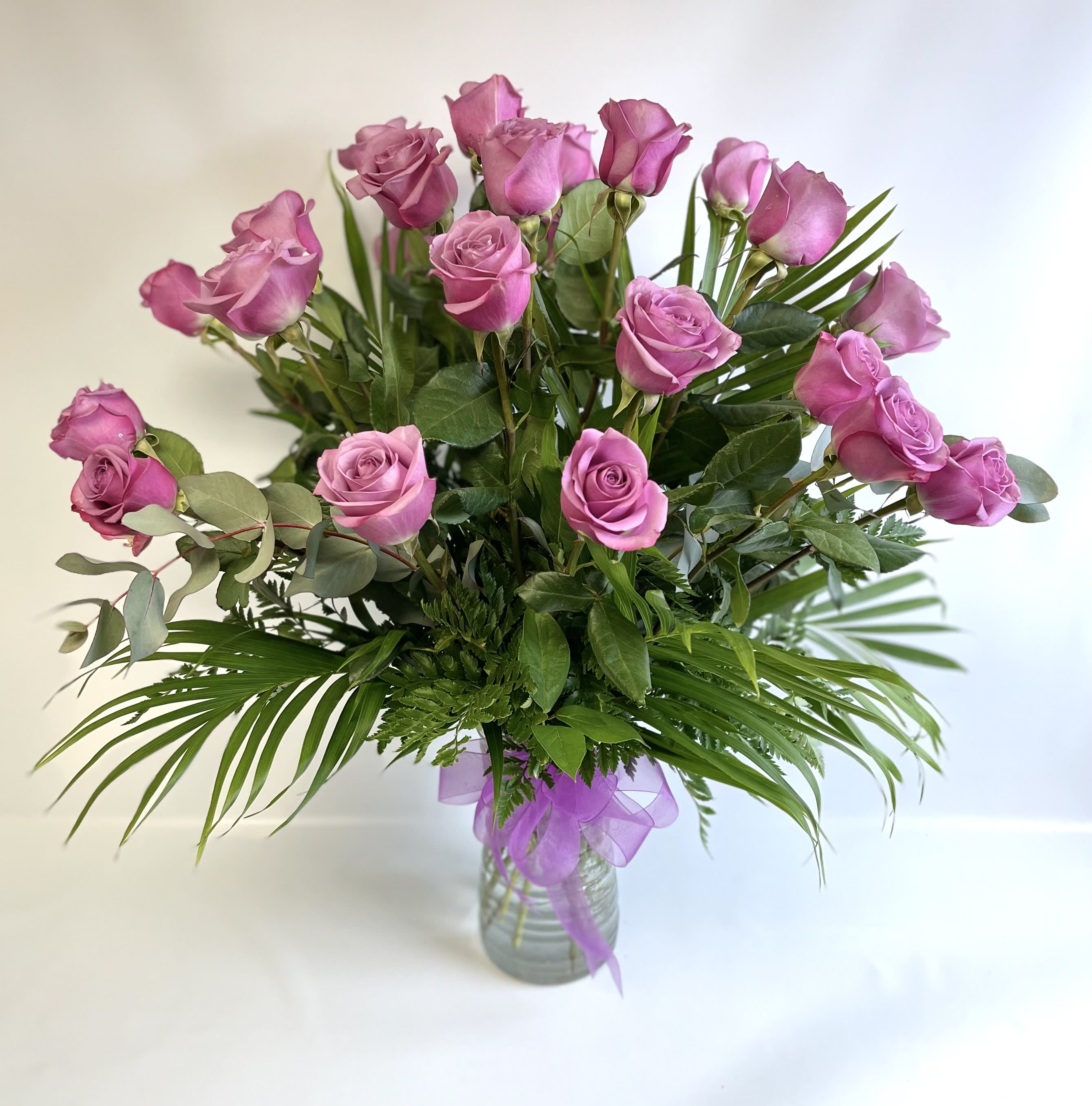 Pink roses in a glass vase with a purple ribbon