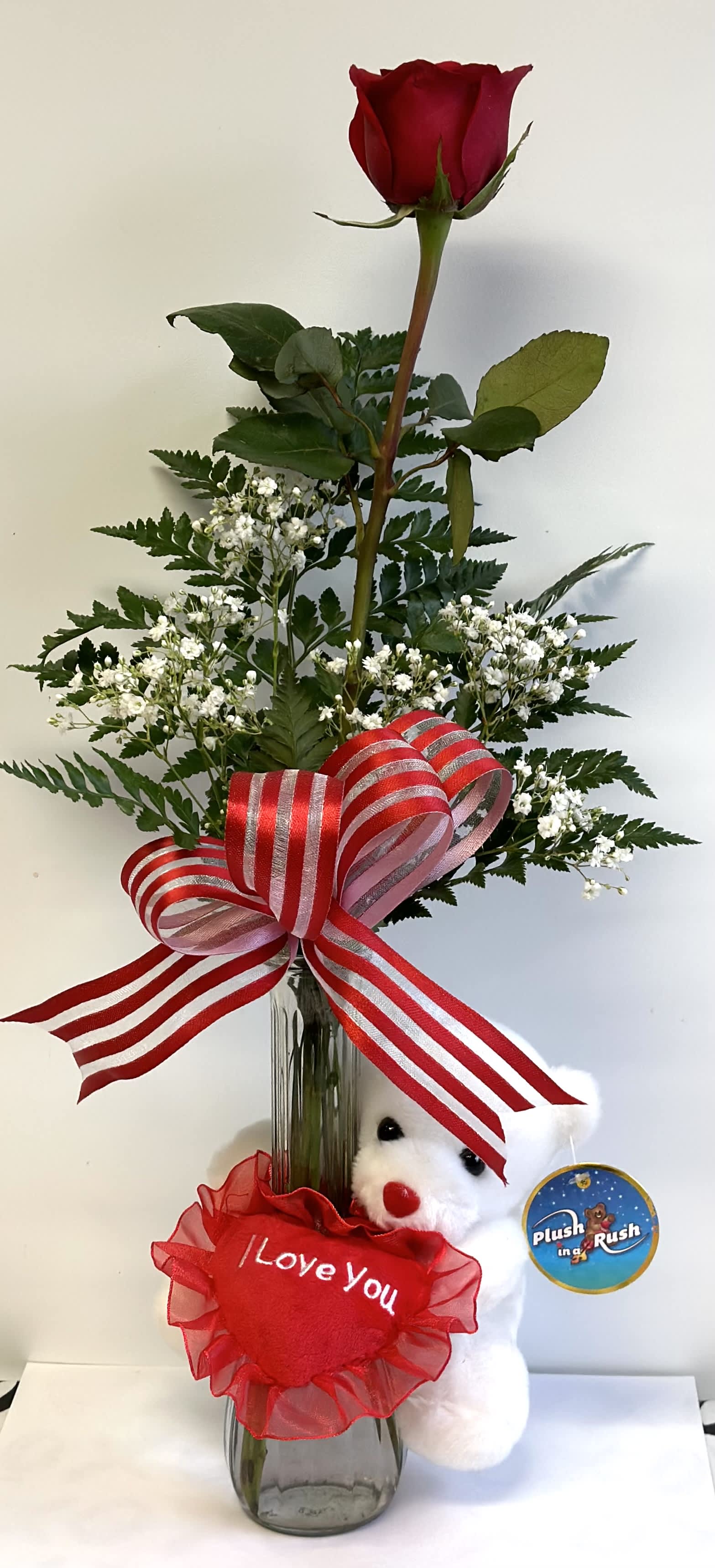 Single red rose in a glass vase with a teddy bear and ribbon bow