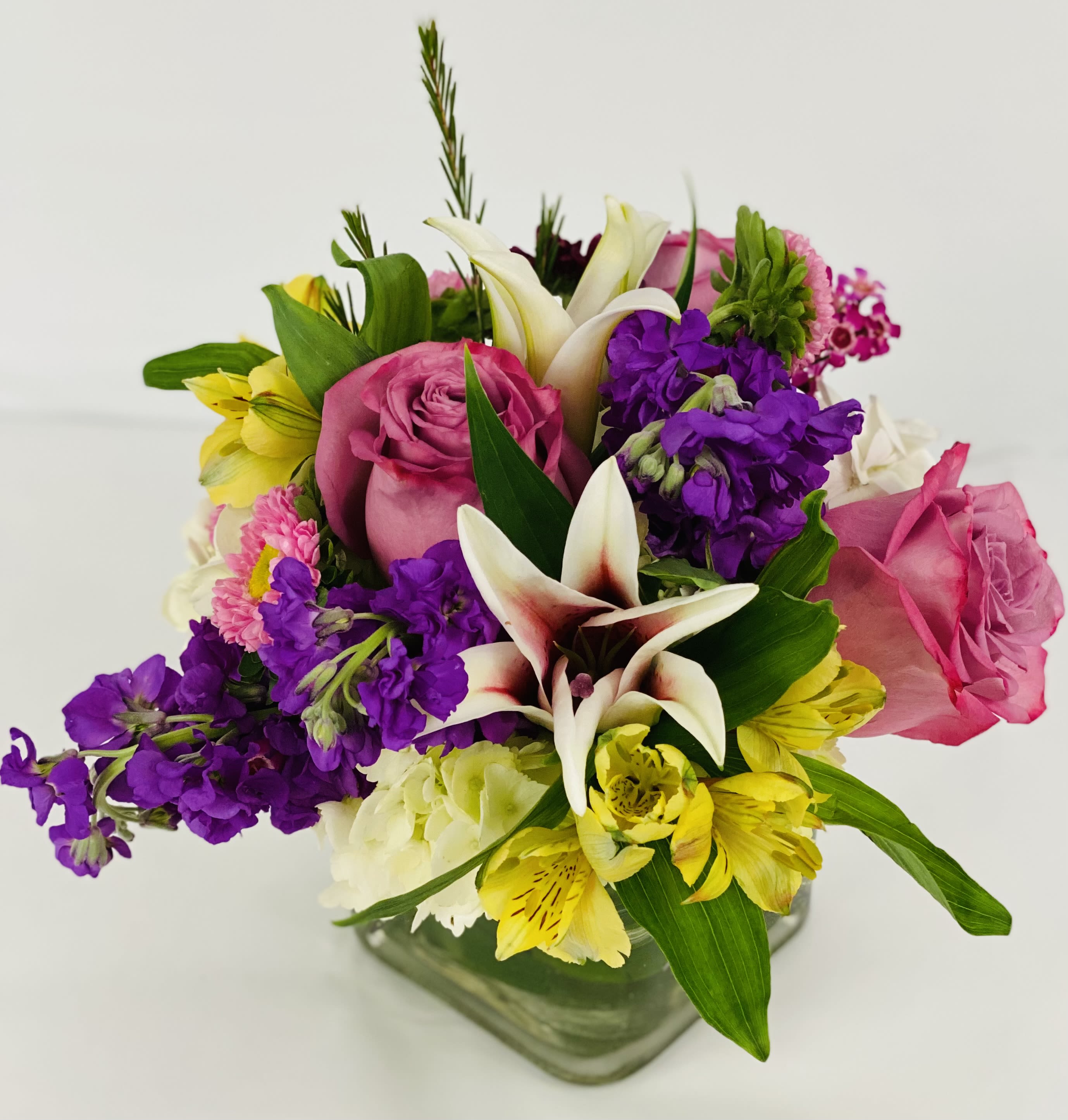 Mixed bouquet with pink roses, white lilies, and purple flowers in a glass vase