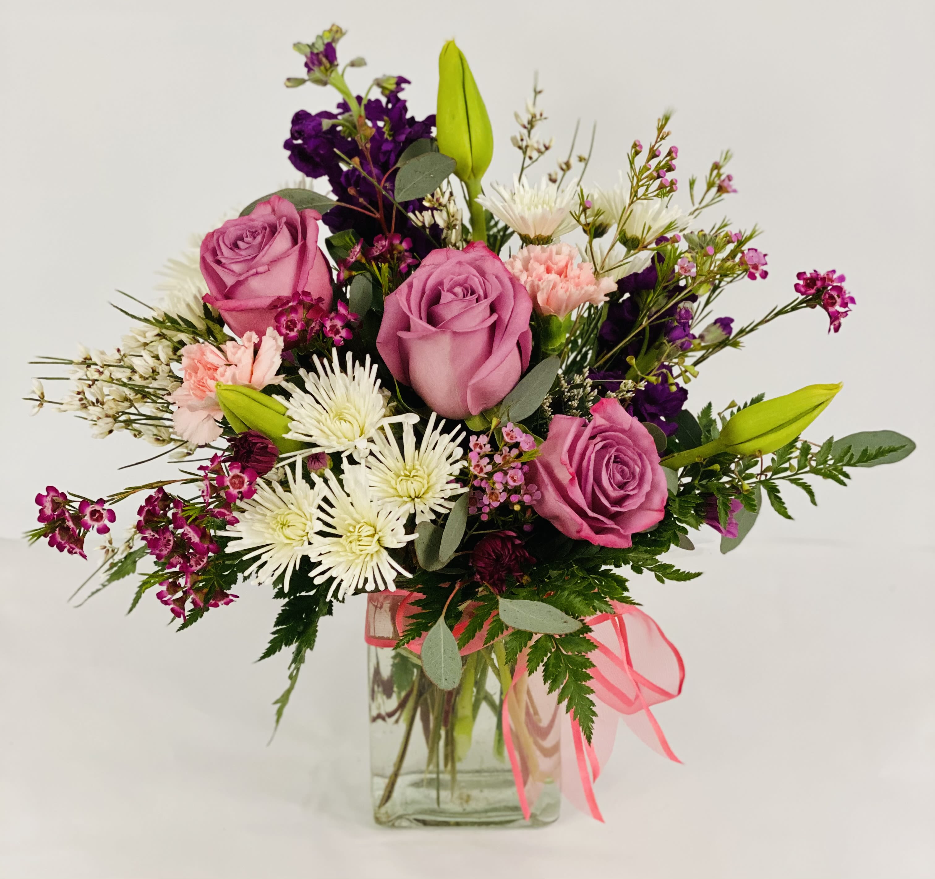 Pink roses and mixed flowers in a clear glass vase with a pink ribbon