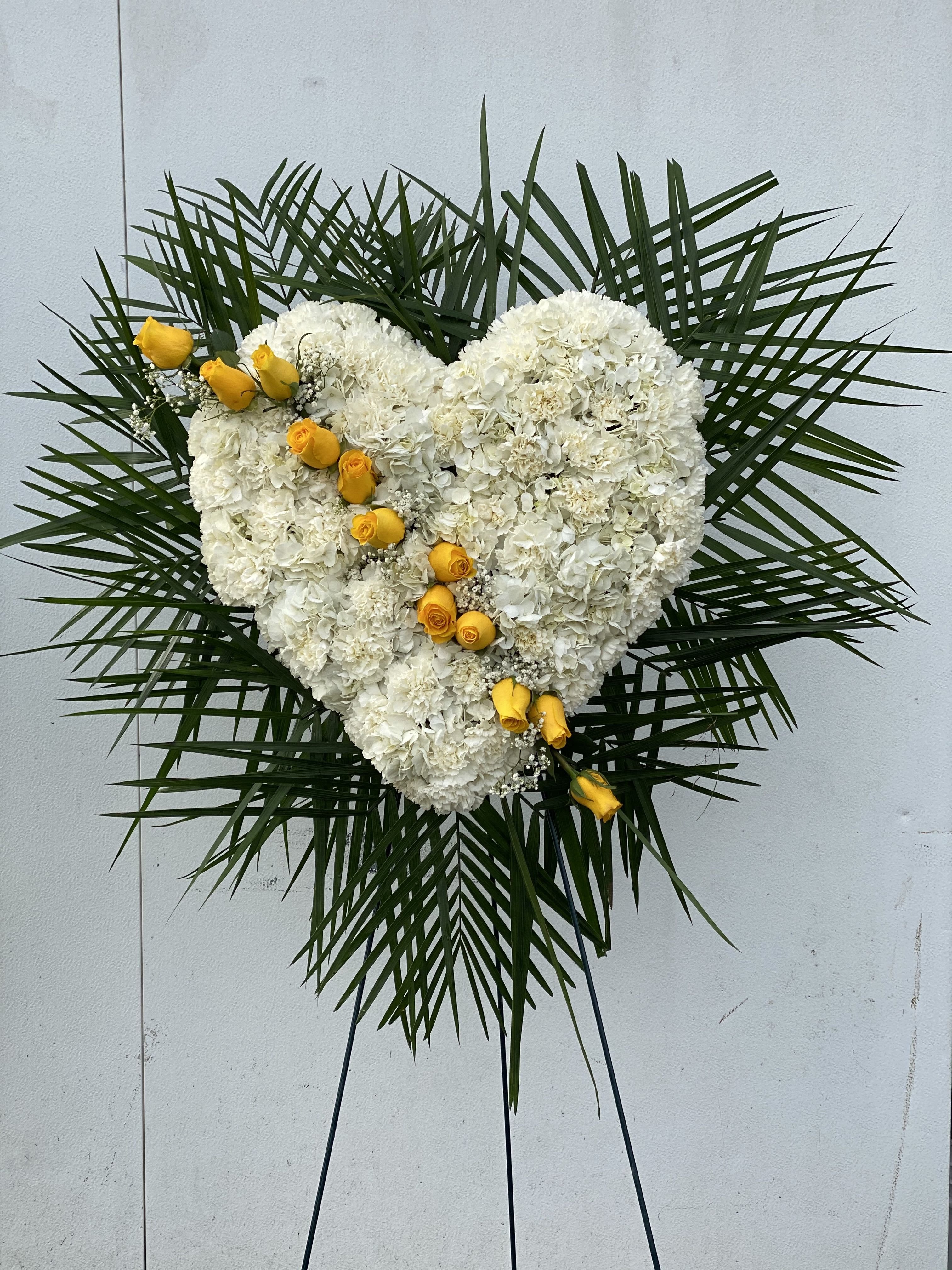 Heart-shaped white floral spray with yellow roses on a stand