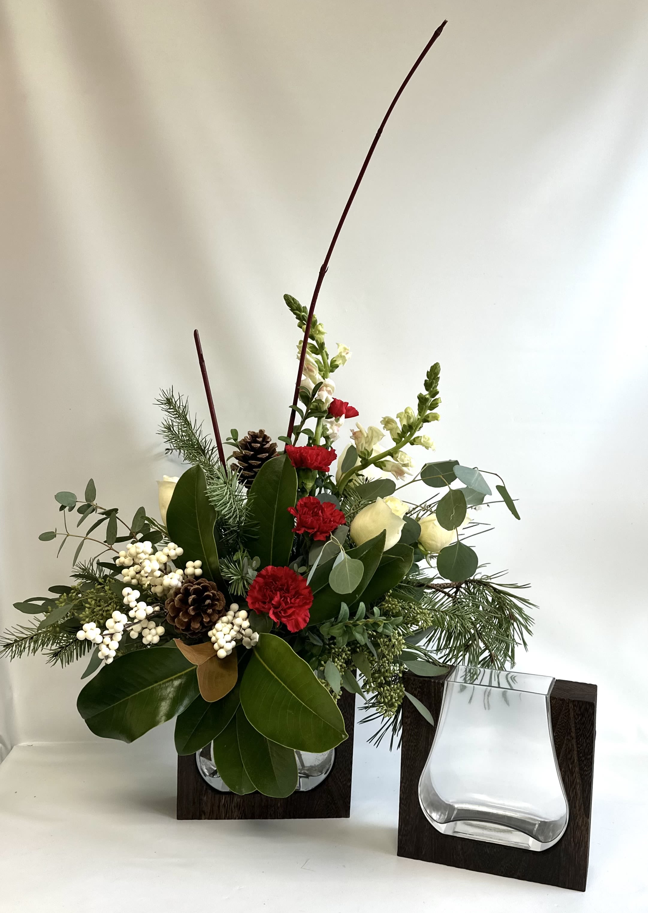 Holiday floral arrangement with red carnations, white blooms, pinecones, and greenery in a glass vase