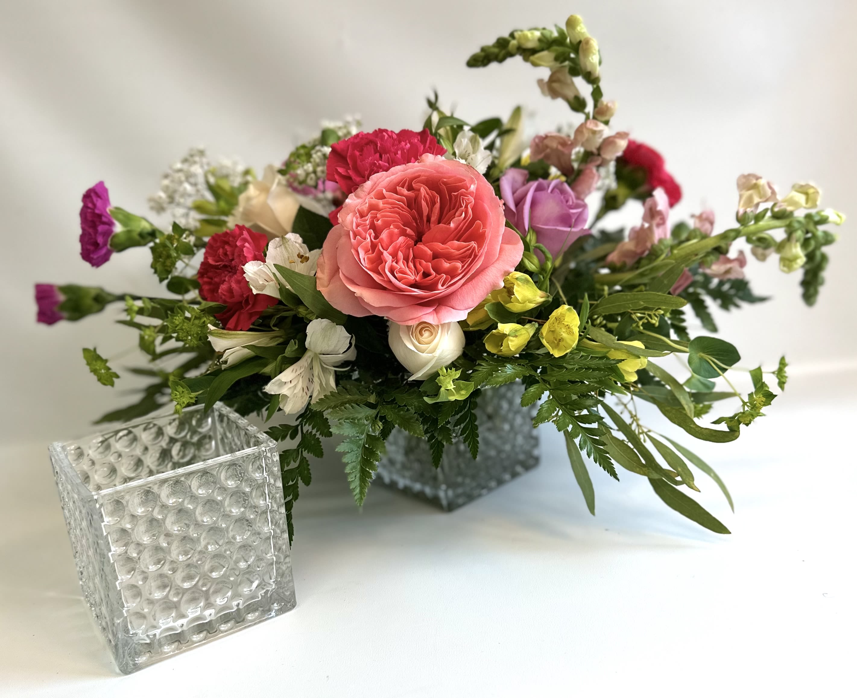 Mixed bouquet in a square glass vase with pink, red, purple, and yellow flowers