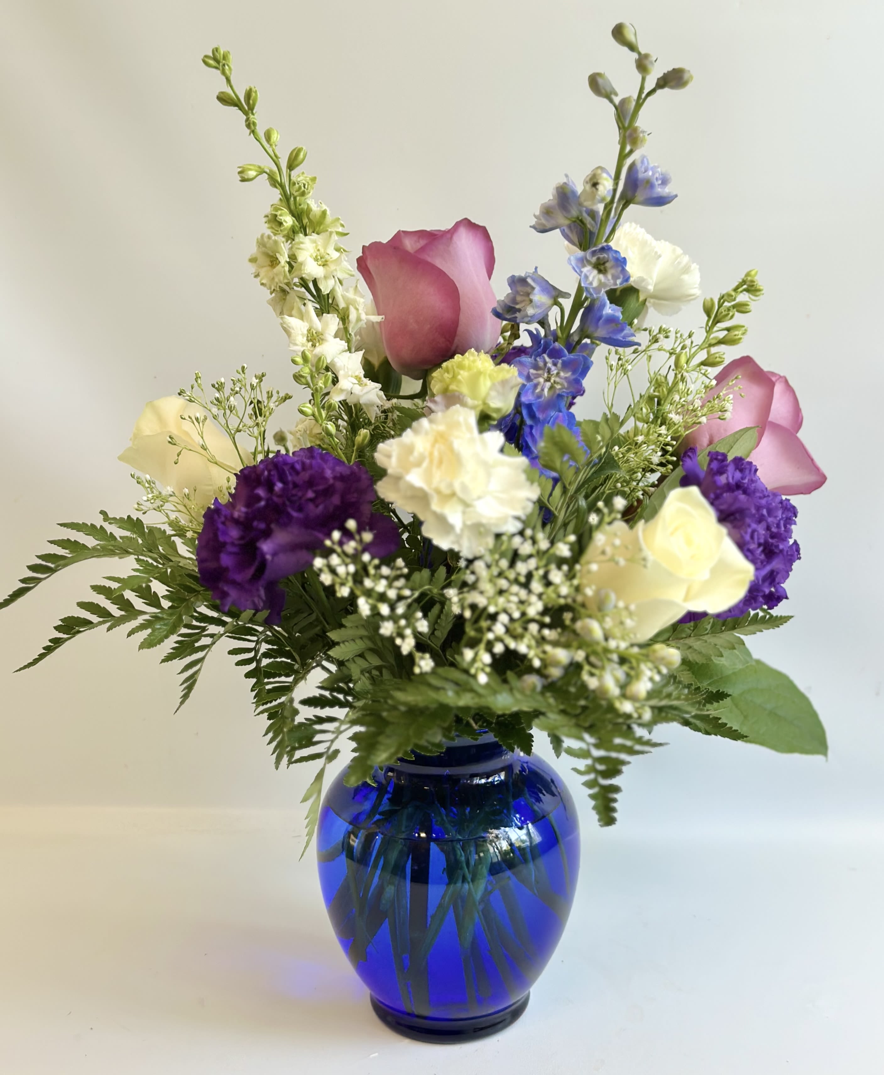 Mixed bouquet in a blue glass vase with pink, purple, white, and yellow flowers