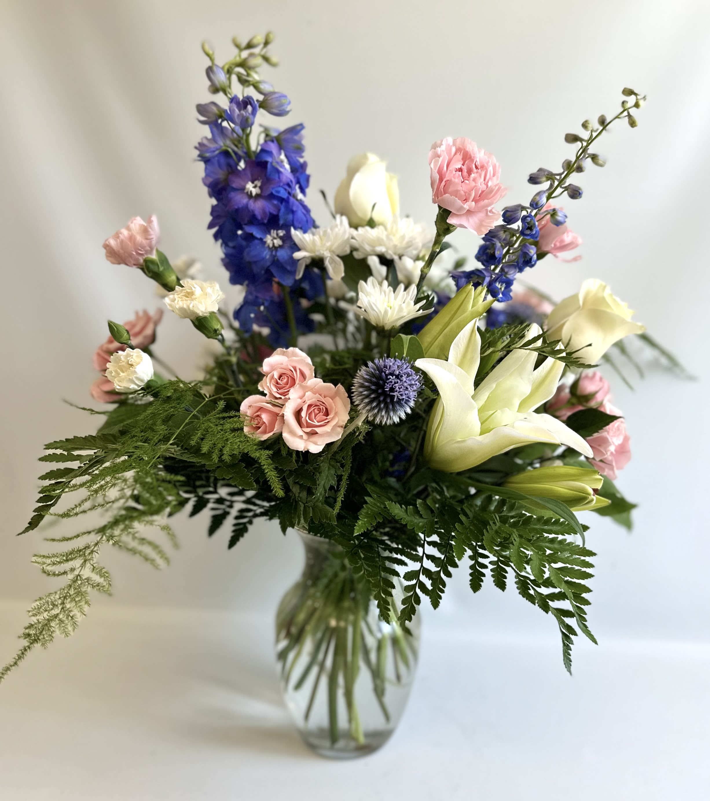 Mixed bouquet of pink, white, and blue flowers in a glass vase
