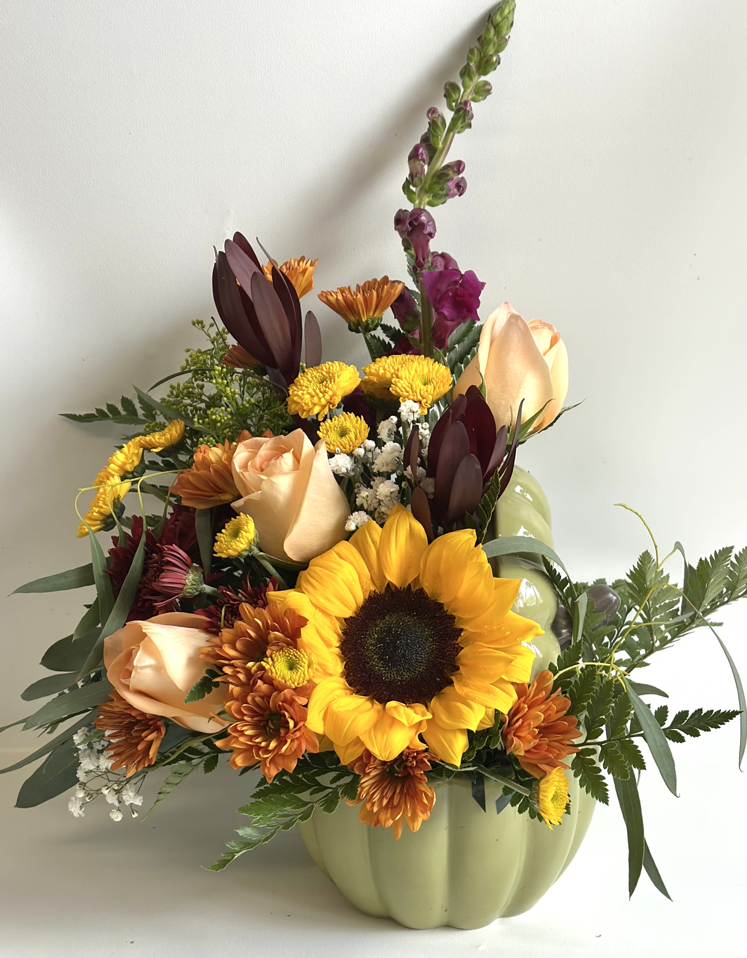 Mixed bouquet in a pale green pumpkin vase with a sunflower and peach roses