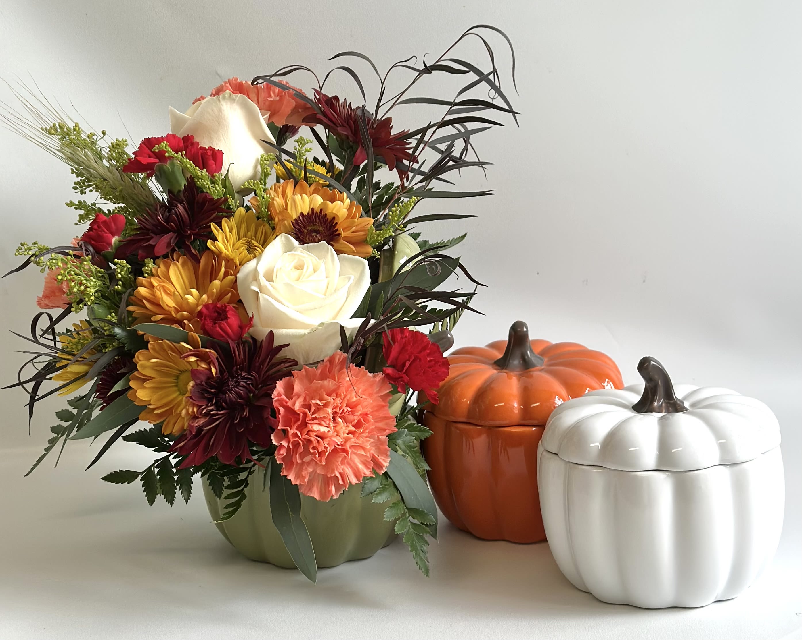 Mixed autumn bouquet in a green vase beside two pumpkin containers