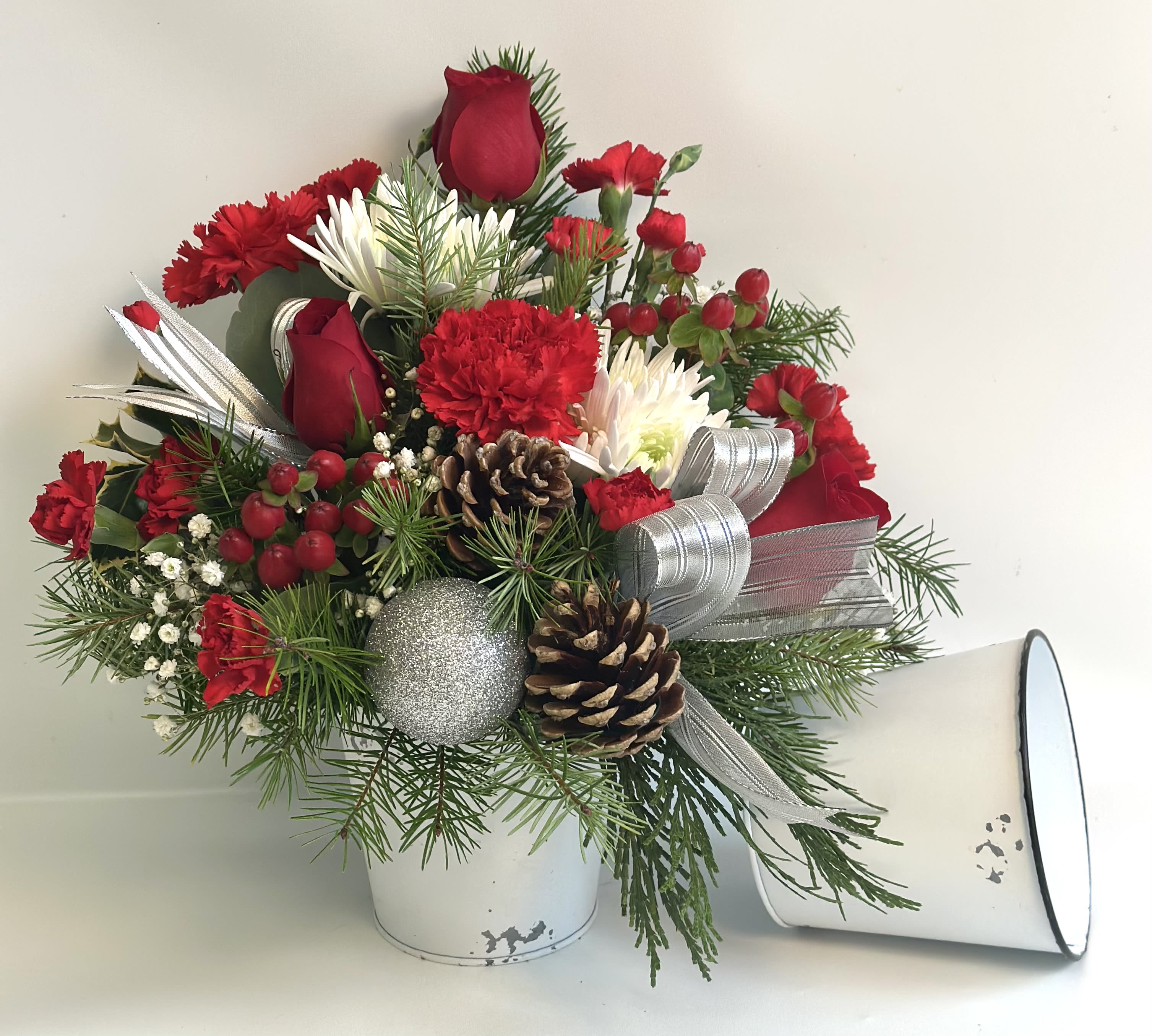 Red and white floral arrangement in a white container with pinecones and ribbon