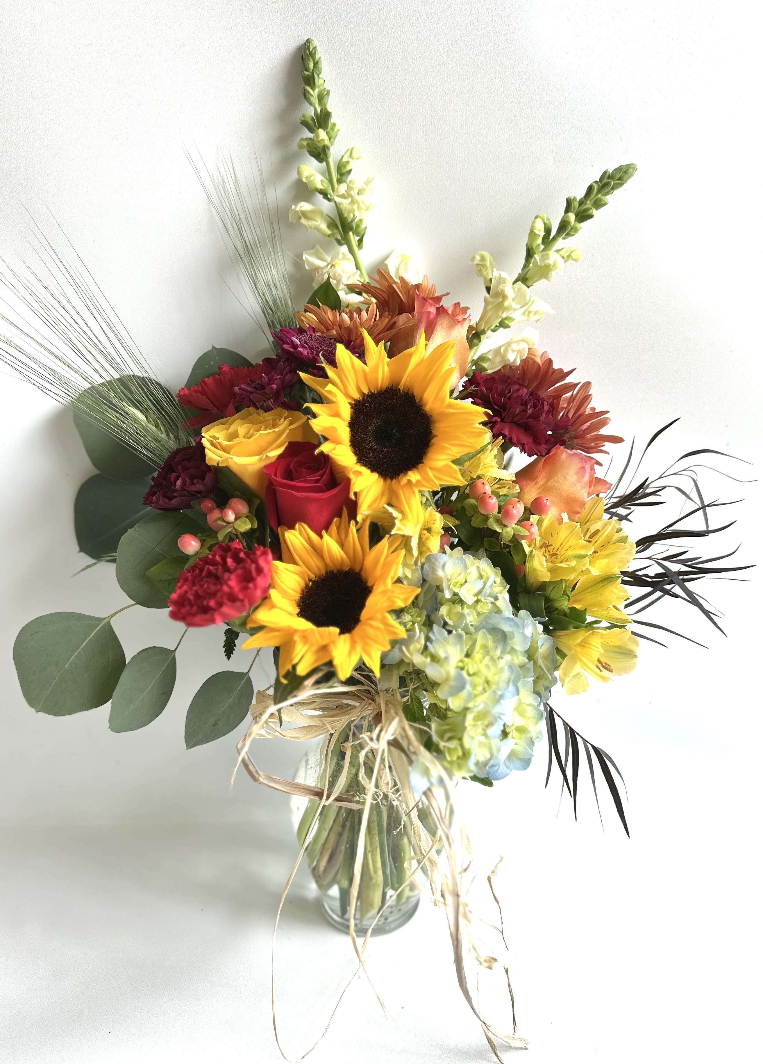 Bouquet of sunflowers, roses, hydrangea, and mixed blooms in a glass vase
