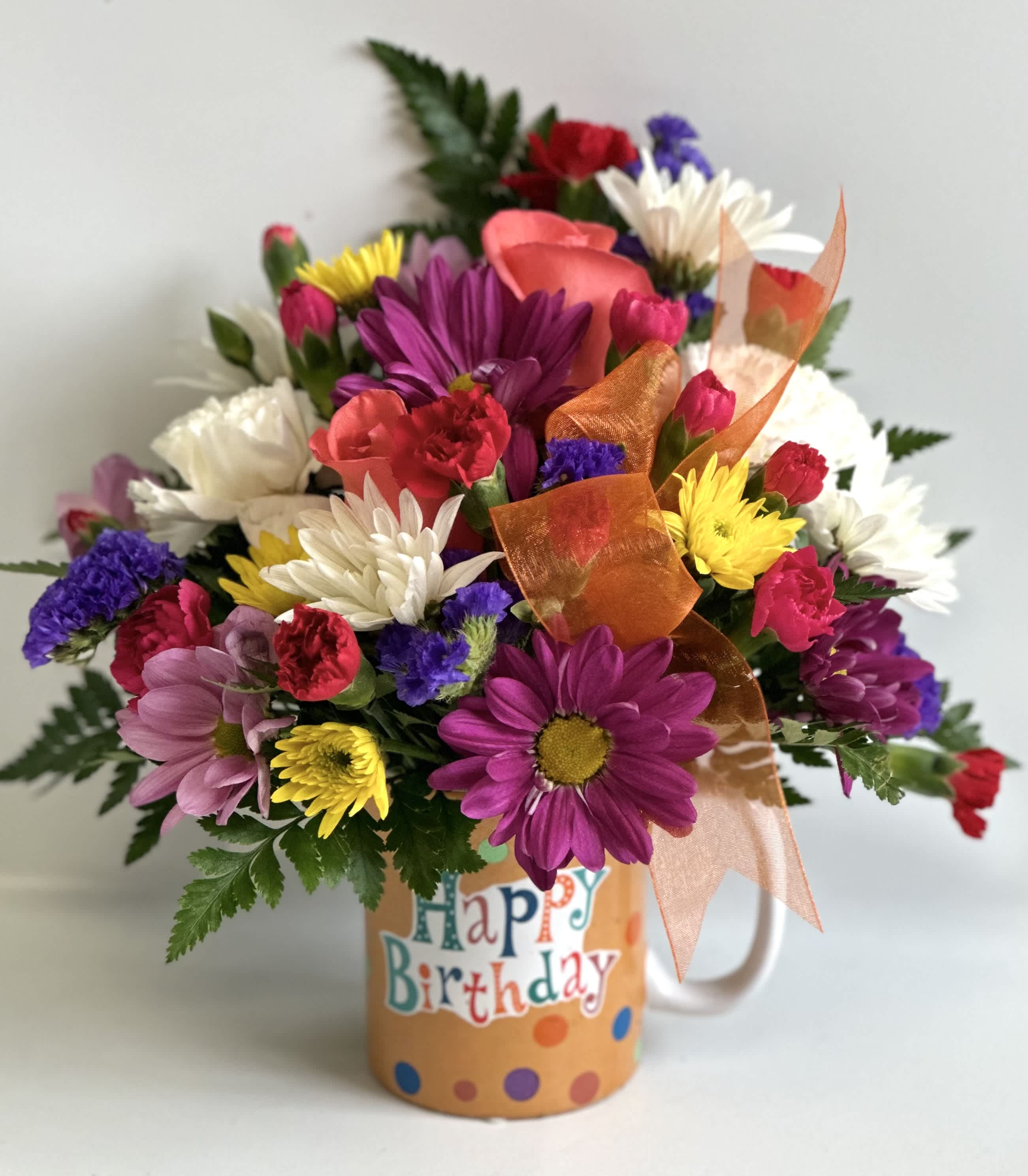 Colorful mixed flower bouquet in a birthday mug with orange ribbon