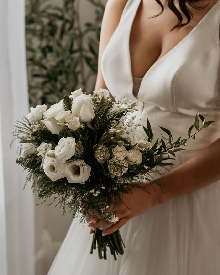 Bride holding a white bouquet with roses and small filler flowers