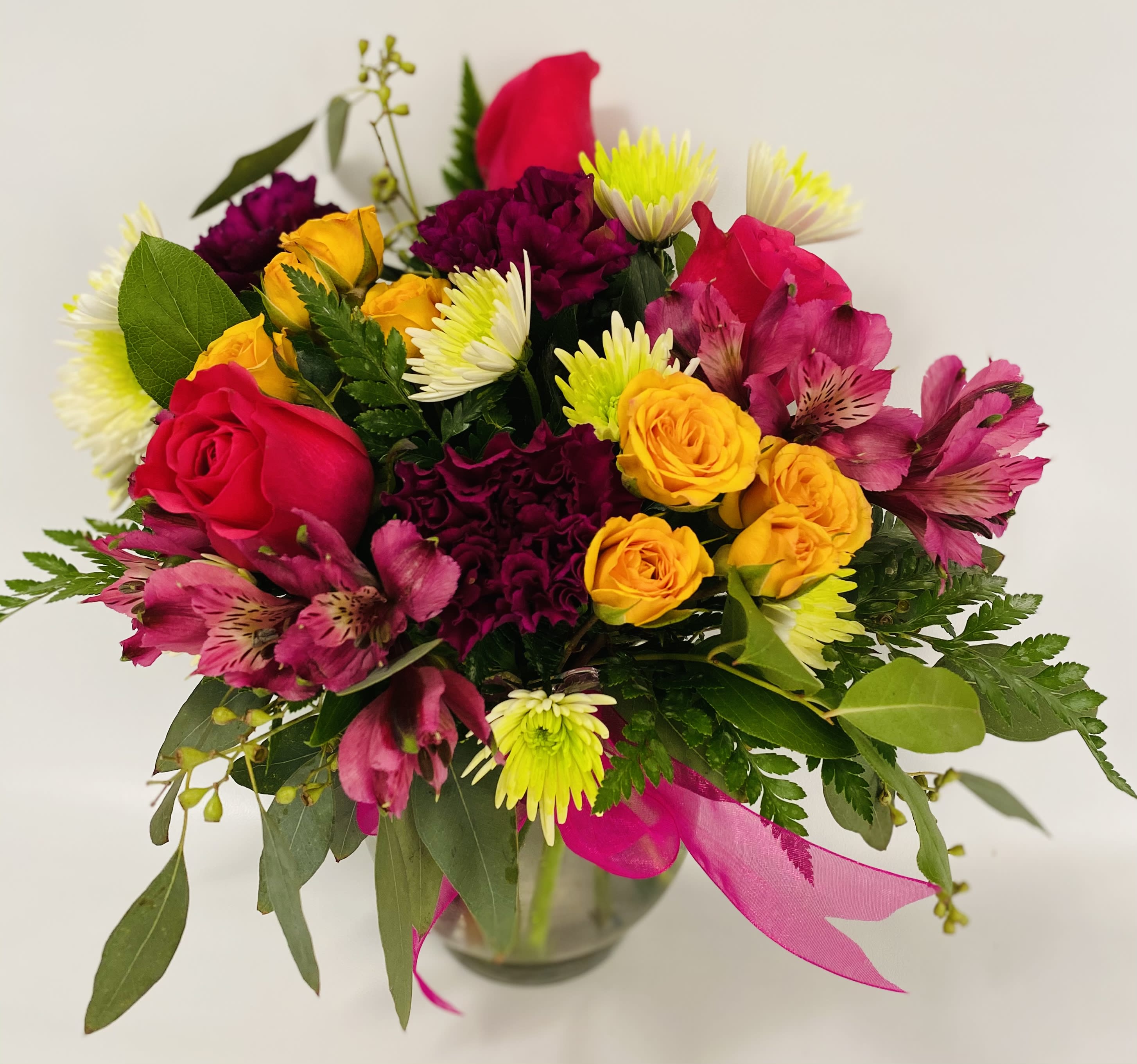 Mixed bouquet of roses and daisies in a glass vase with pink ribbon