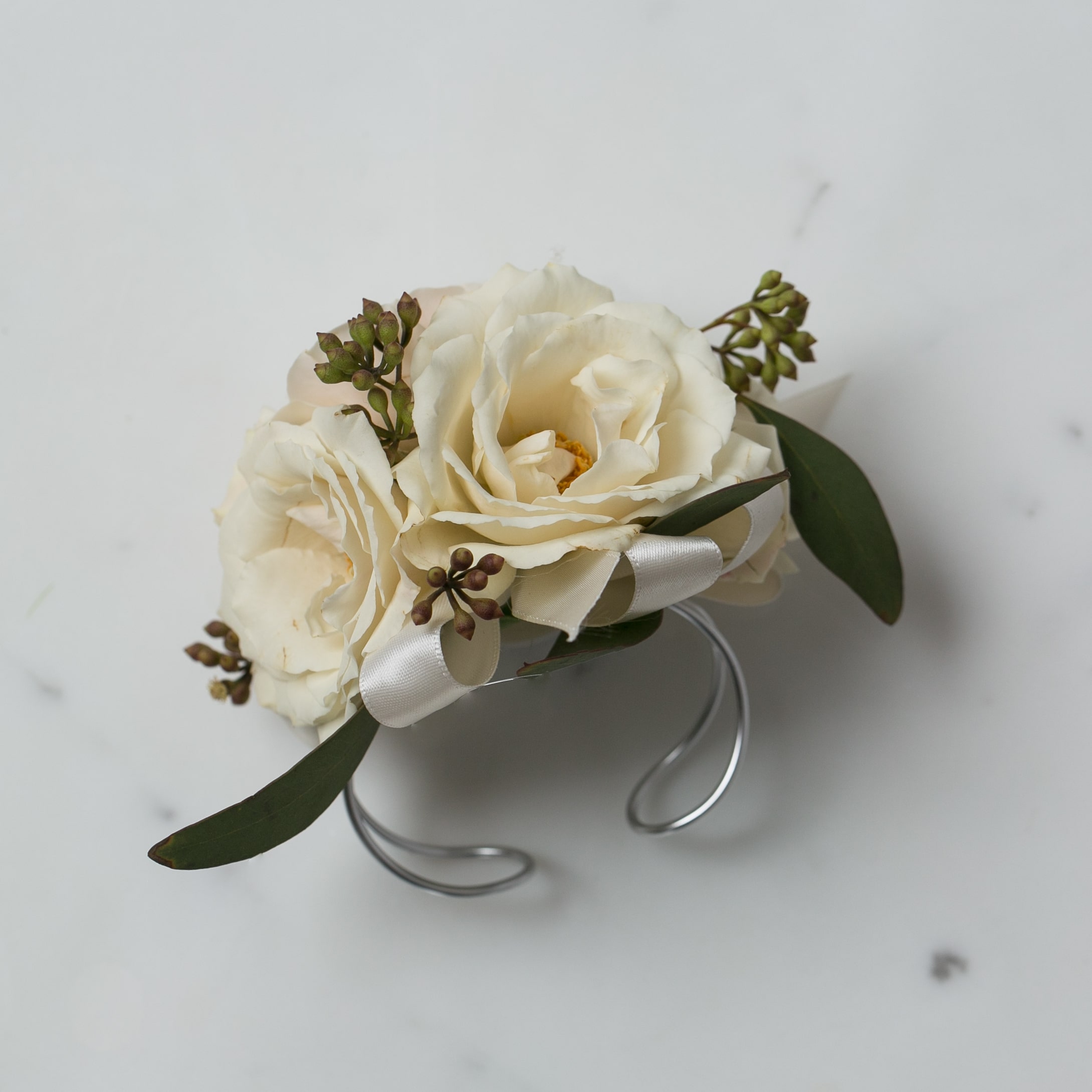 Ivory rose wrist corsage with white ribbon on a silver cuff bracelet.