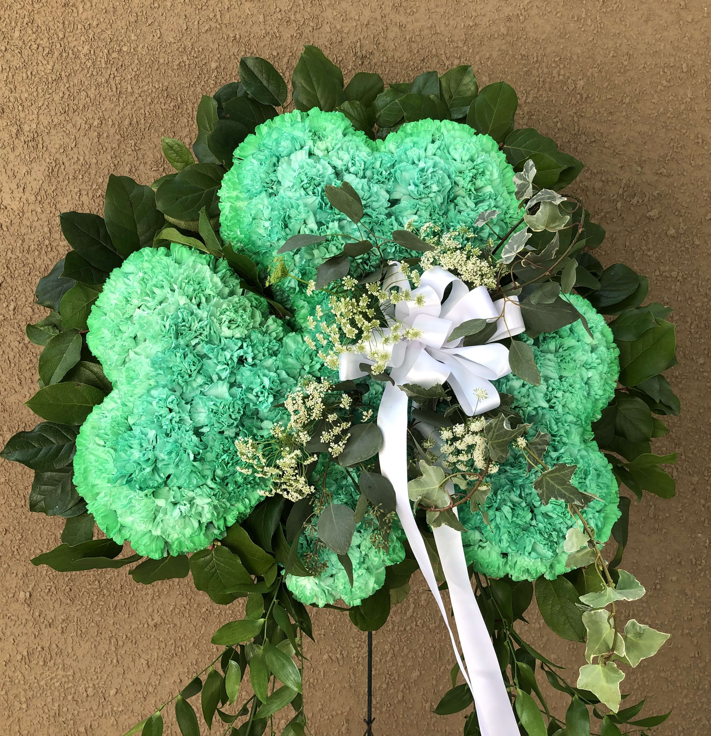Green carnation wreath with white ribbon and dark foliage