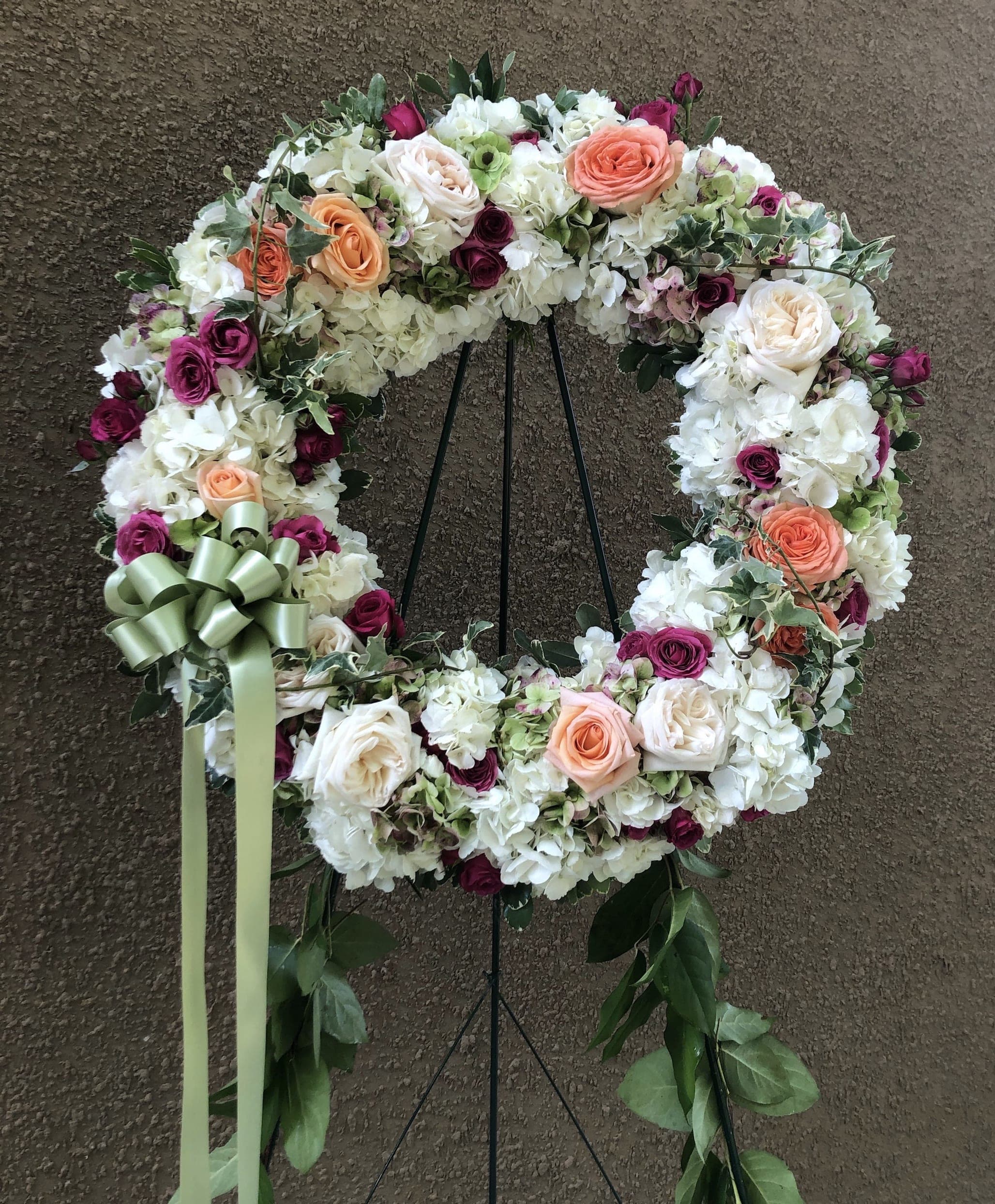 Floral wreath with white, peach, and magenta roses on a stand
