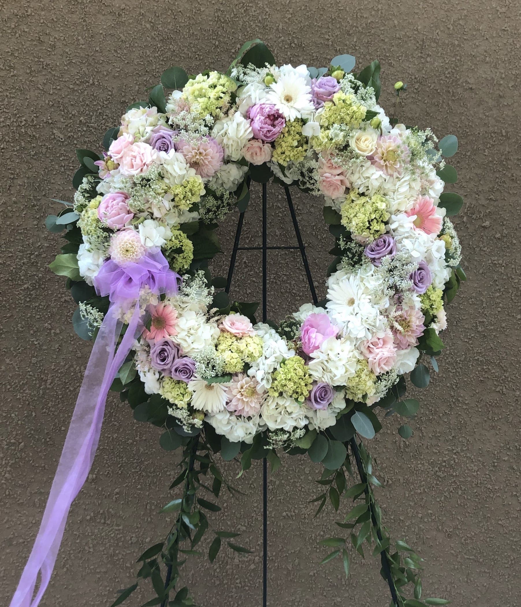 Pastel floral wreath on a stand with a lavender ribbon